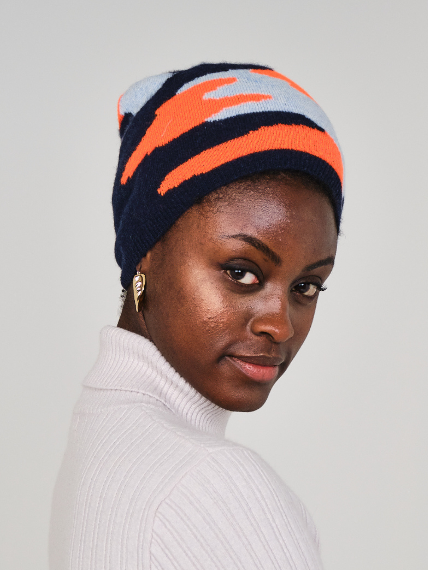 women wearing a navy, orange and light blue camo pattern hat with a pom pom