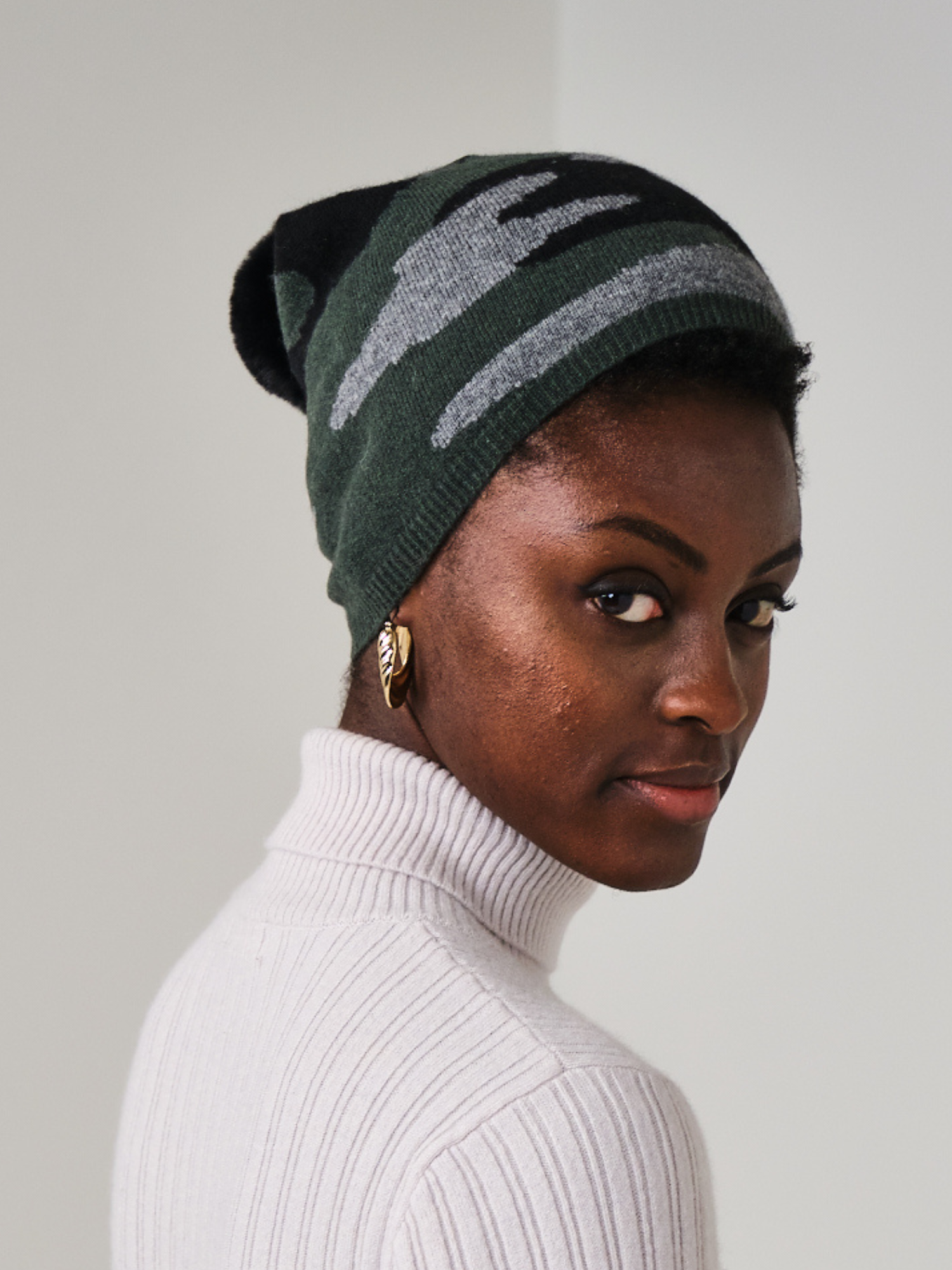 women wearing a khaki, grey and black camo pattern hat with a pom pom