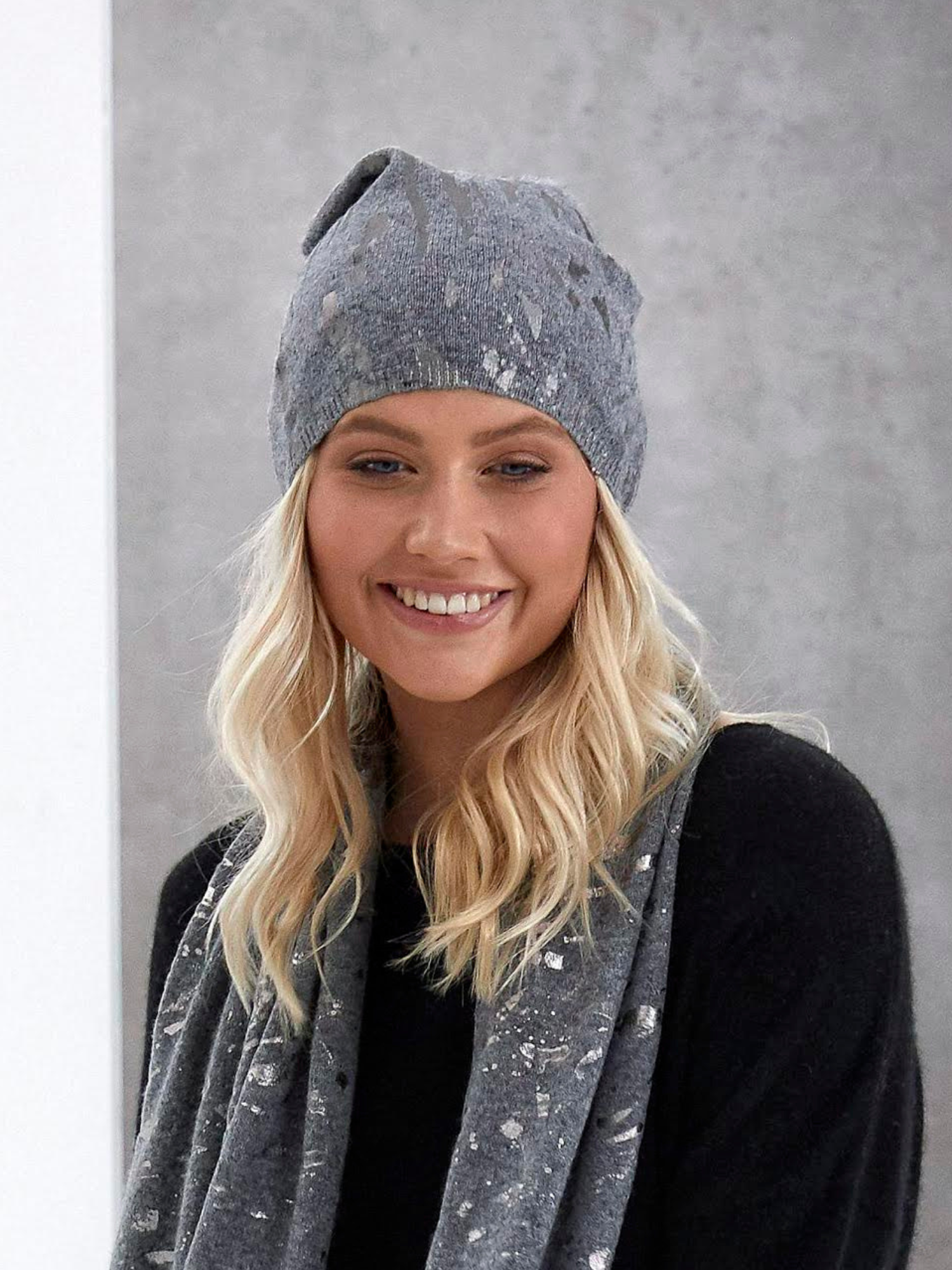 Woman wearing a gray knit hat and scarf against a gray background