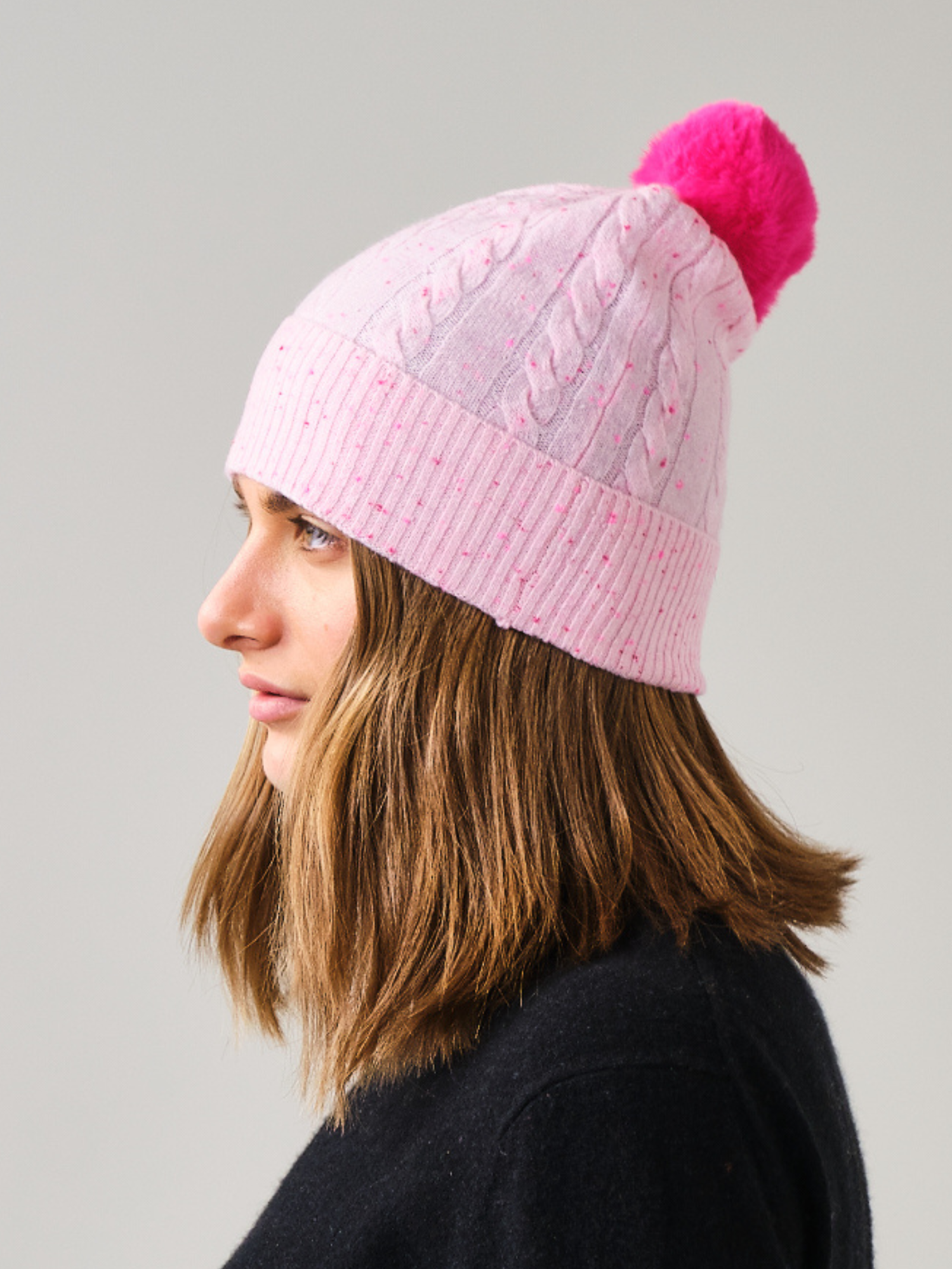 Person wearing a pink knit beanie with a pom-pom on a grey background