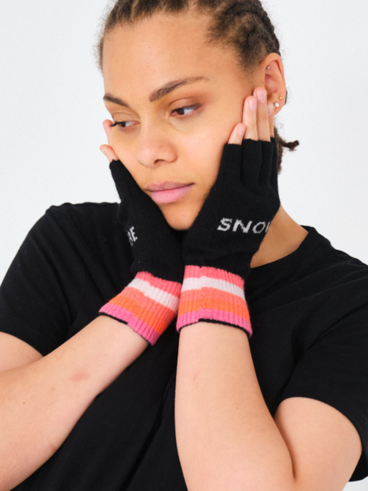 Person wearing black gloves with colorful cuffs and a black shirt on a light gray background