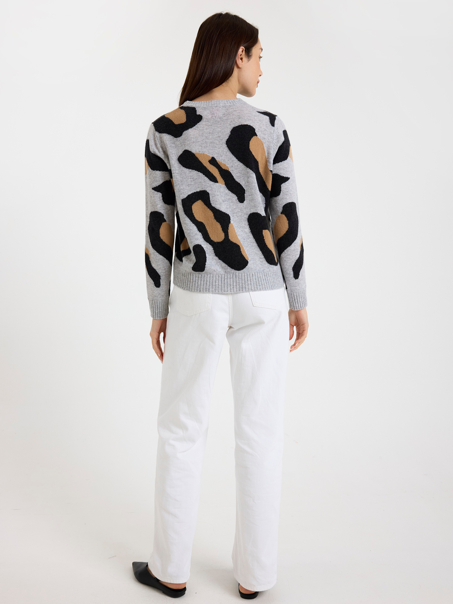 Woman wearing a grey sweater with a leopard print pattern and white jeans on a white background