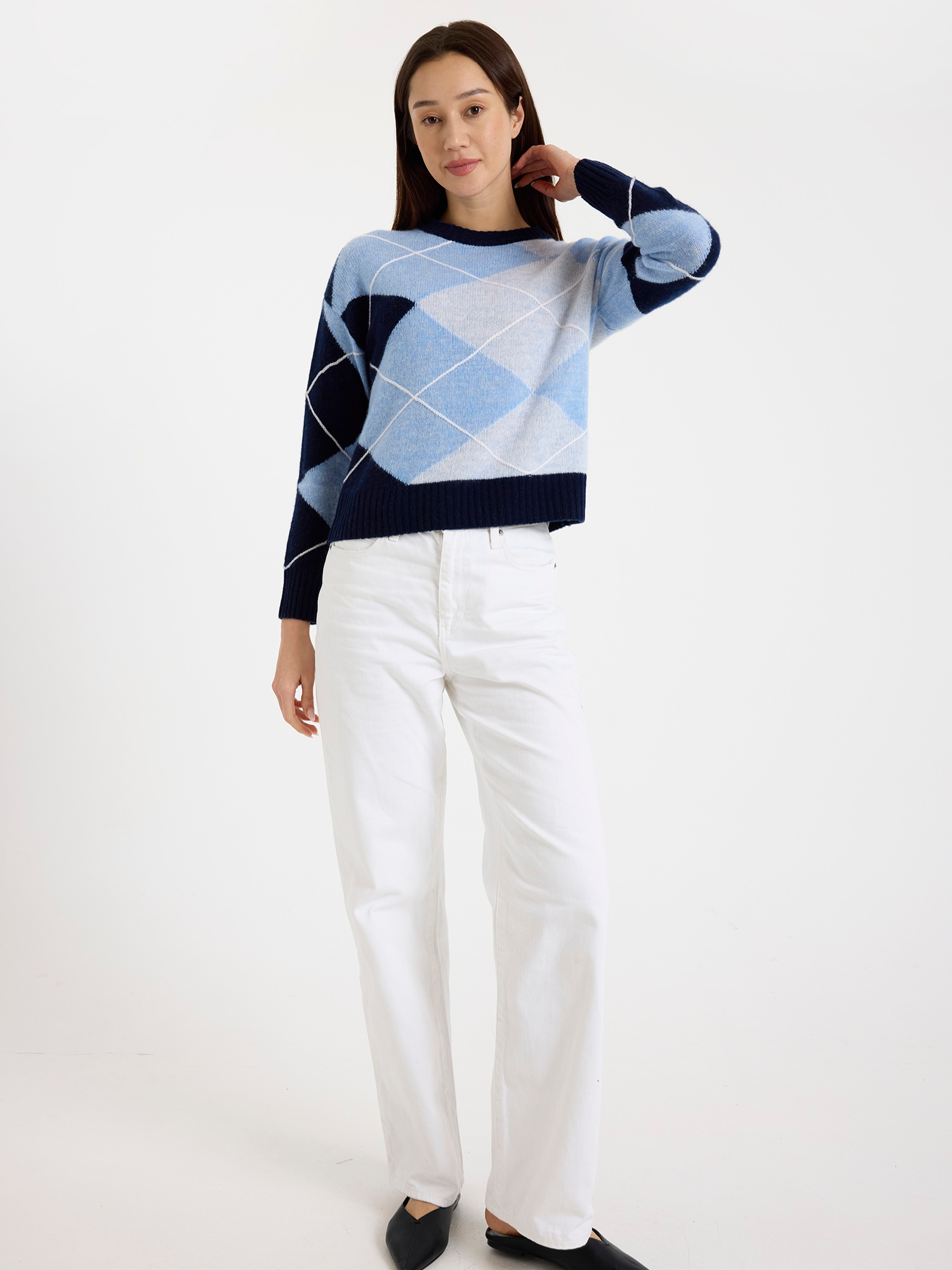 Woman wearing a blue and white argyle sweater with white jeans on a white background