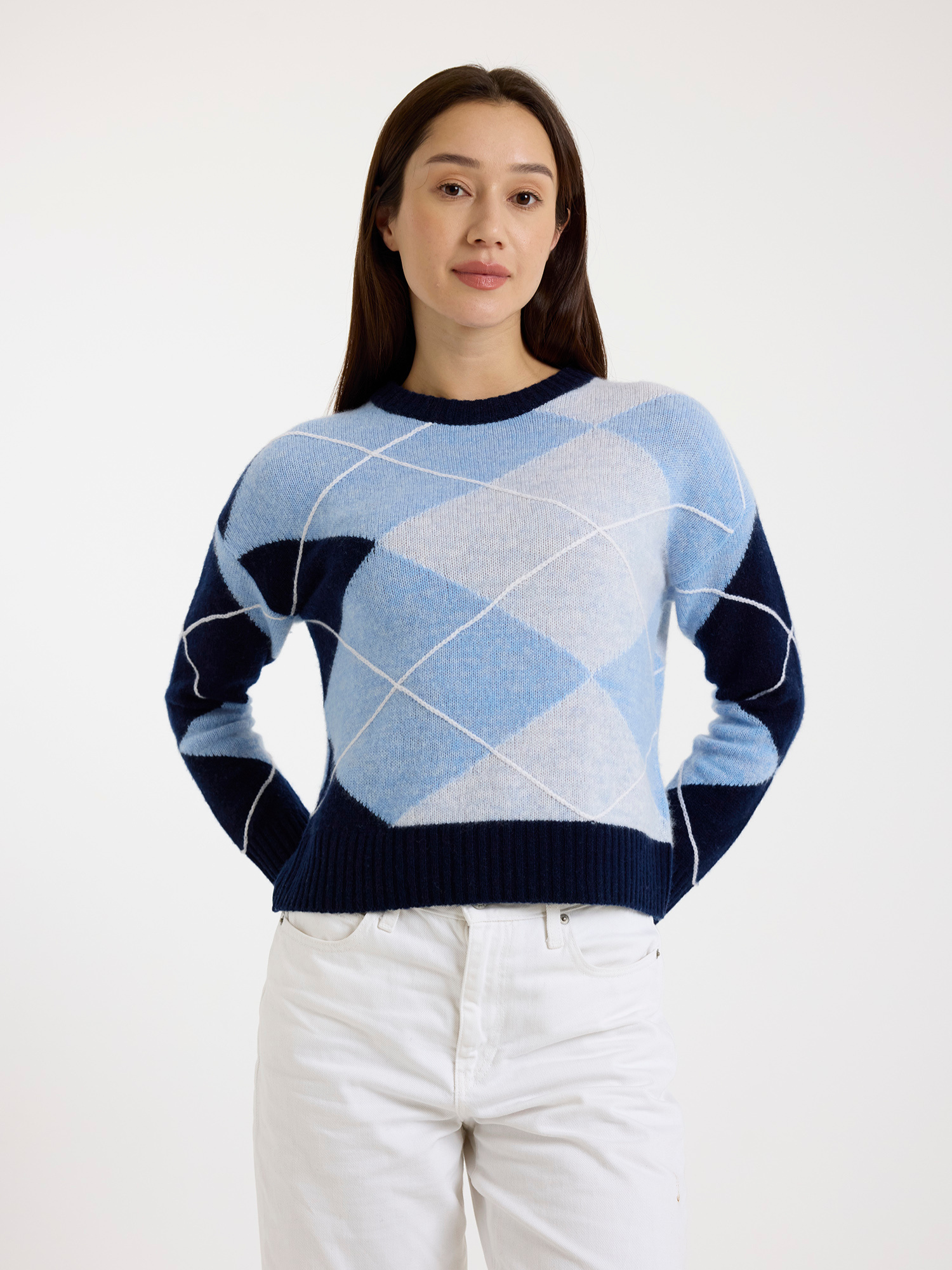 Woman wearing a blue and white argyle sweater with white jeans on a white background