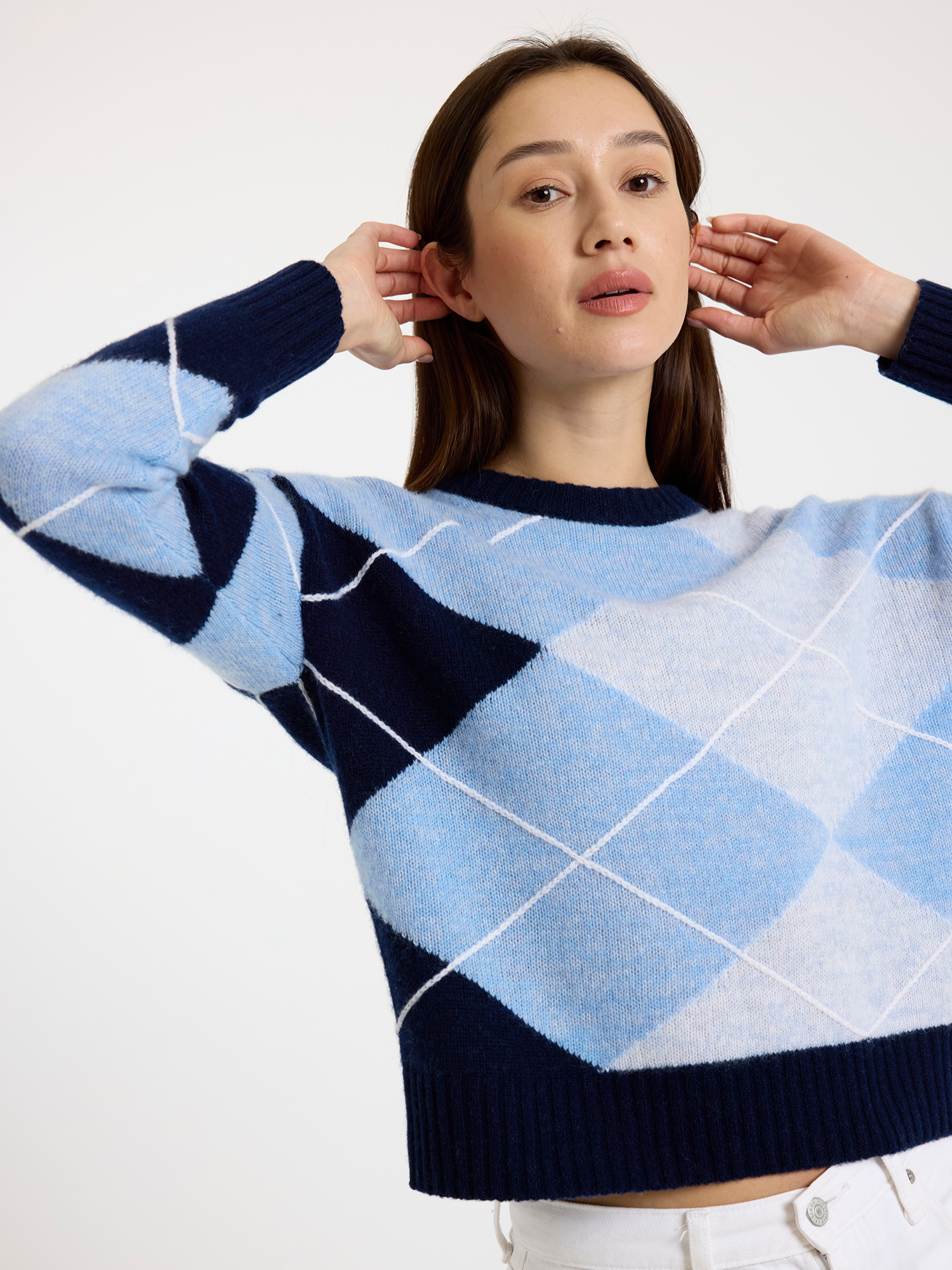 Woman wearing a blue and white argyle sweater on a white background