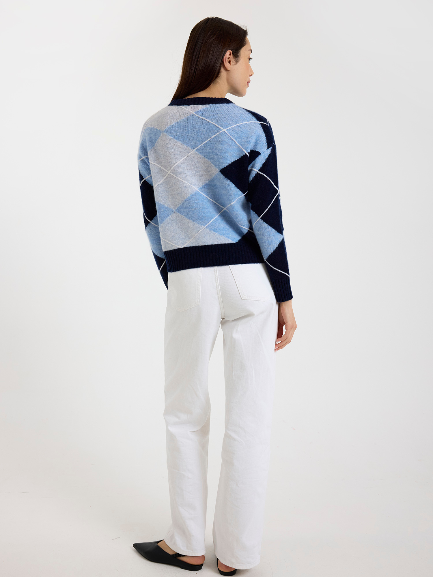 Woman wearing a blue and white argyle sweater with white jeans on a white background