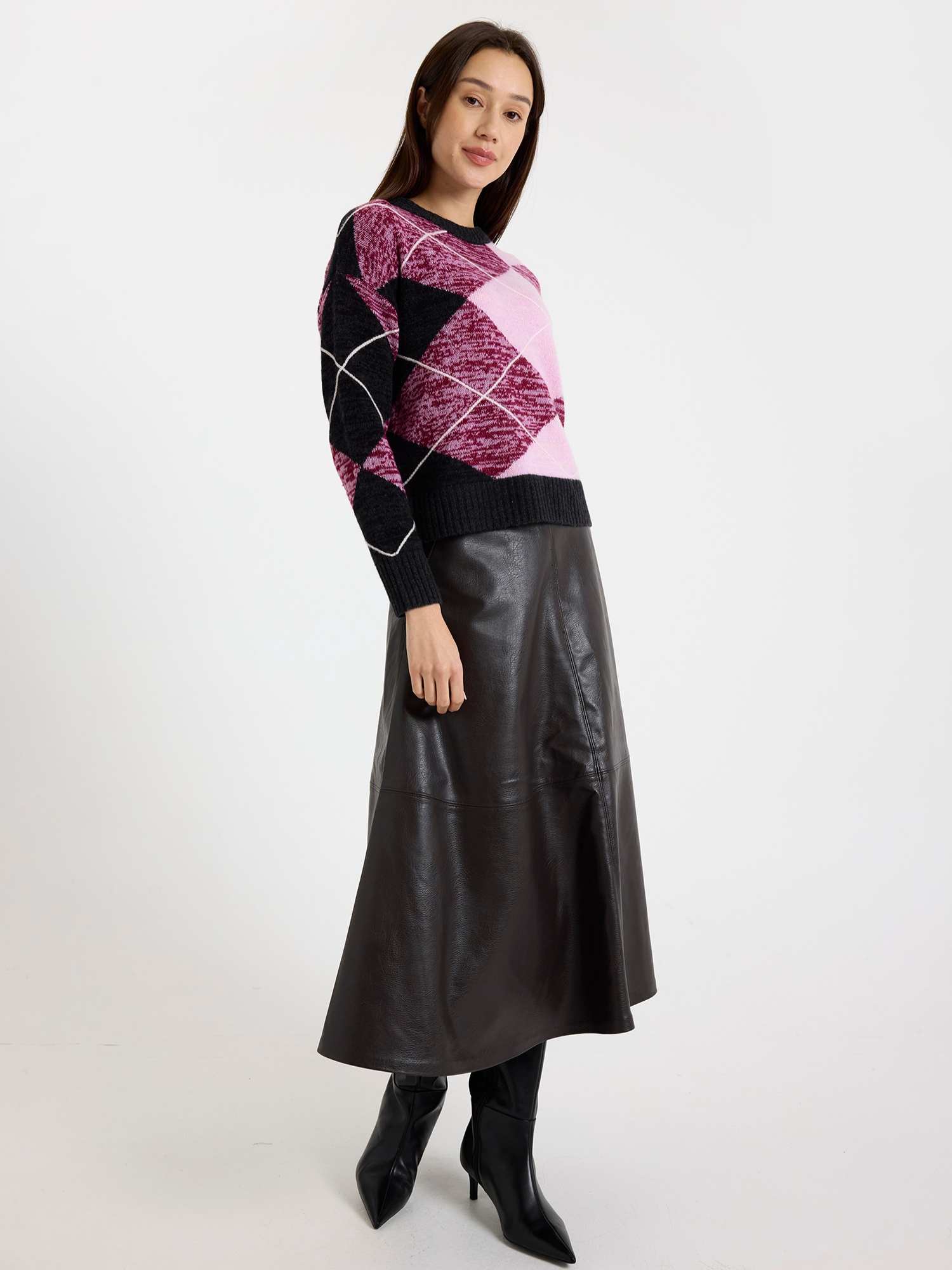 Woman wearing a grey and pink argyle sweater with a brown leather skirt on a white background