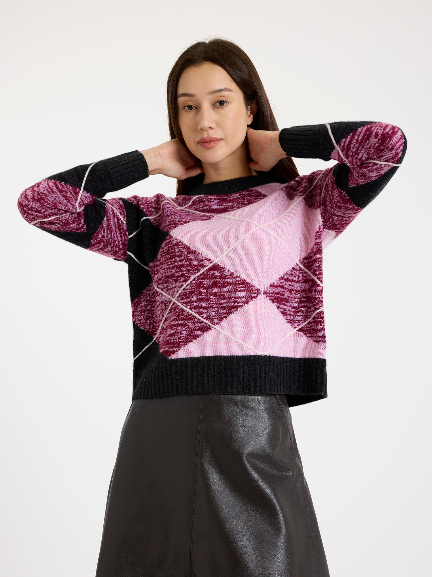 Woman wearing a grey and pink argyle sweater with a brown leather skirt on a white background