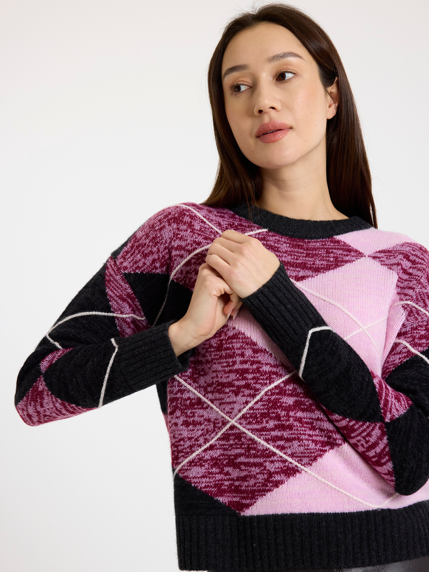 Woman wearing a grey and pink argyle sweater with a brown leather skirt on a white background