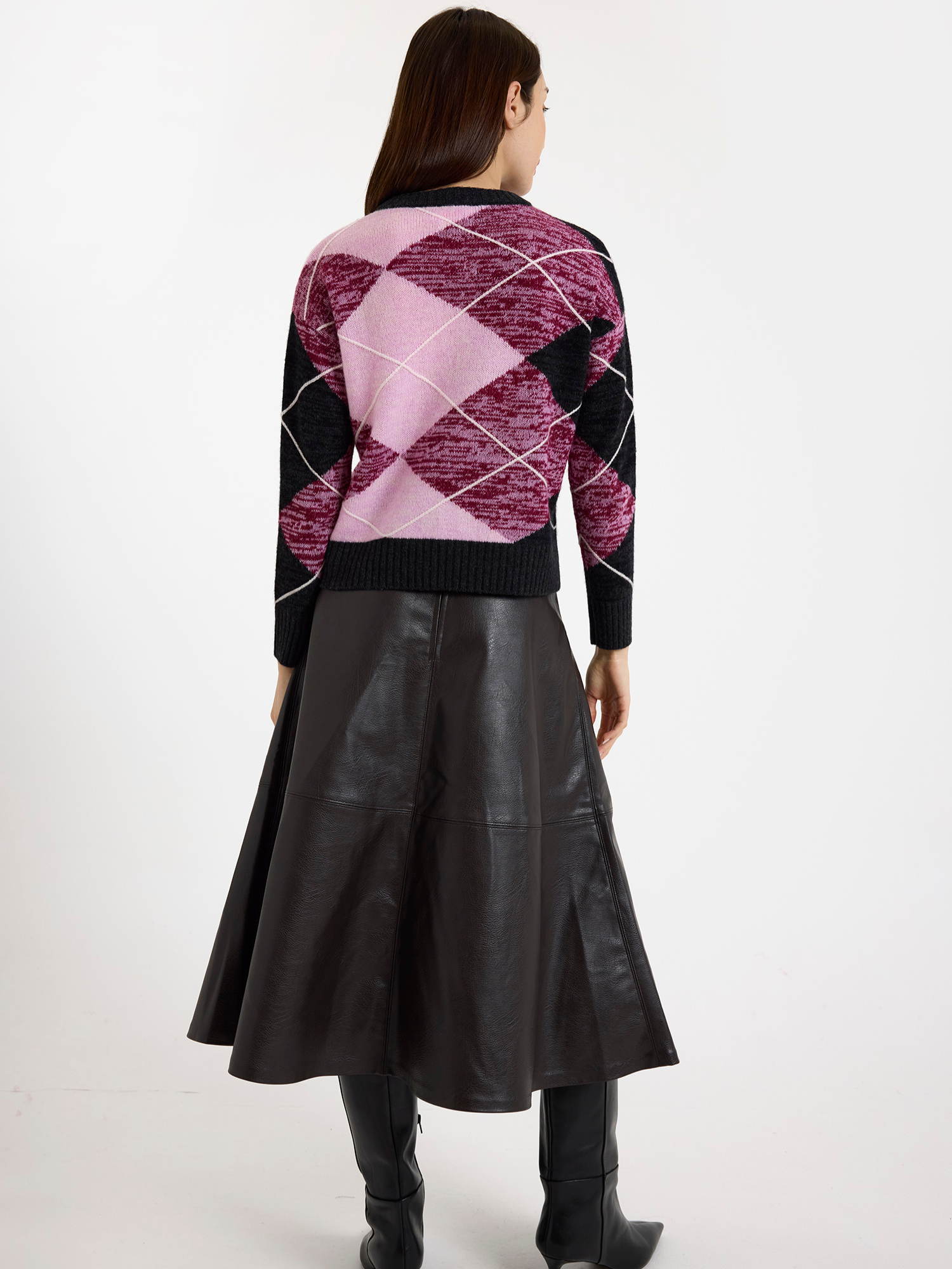 Woman wearing a grey and pink argyle sweater with a brown leather skirt on a white background