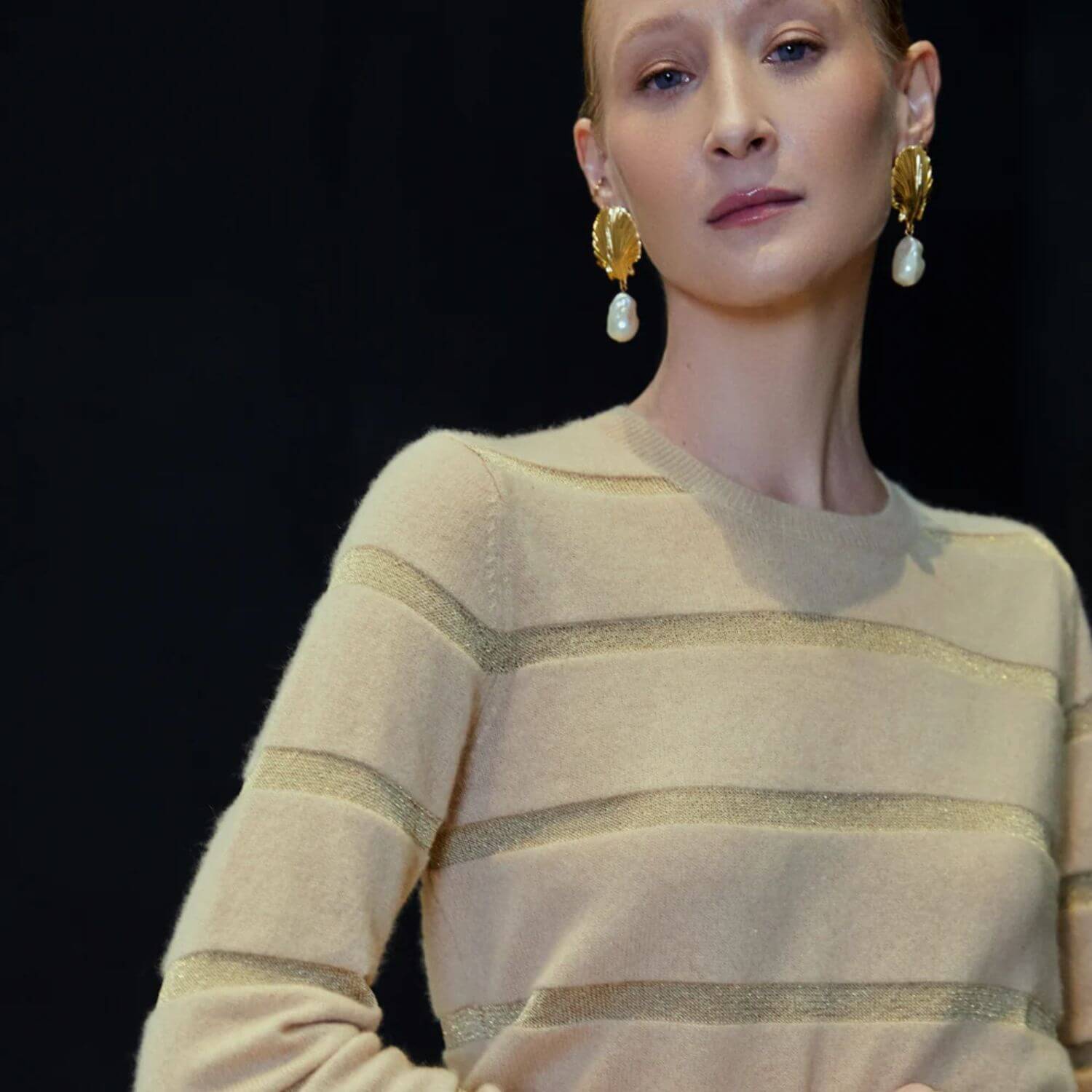 Woman wearing a beige sweater with gold stripes against a black background