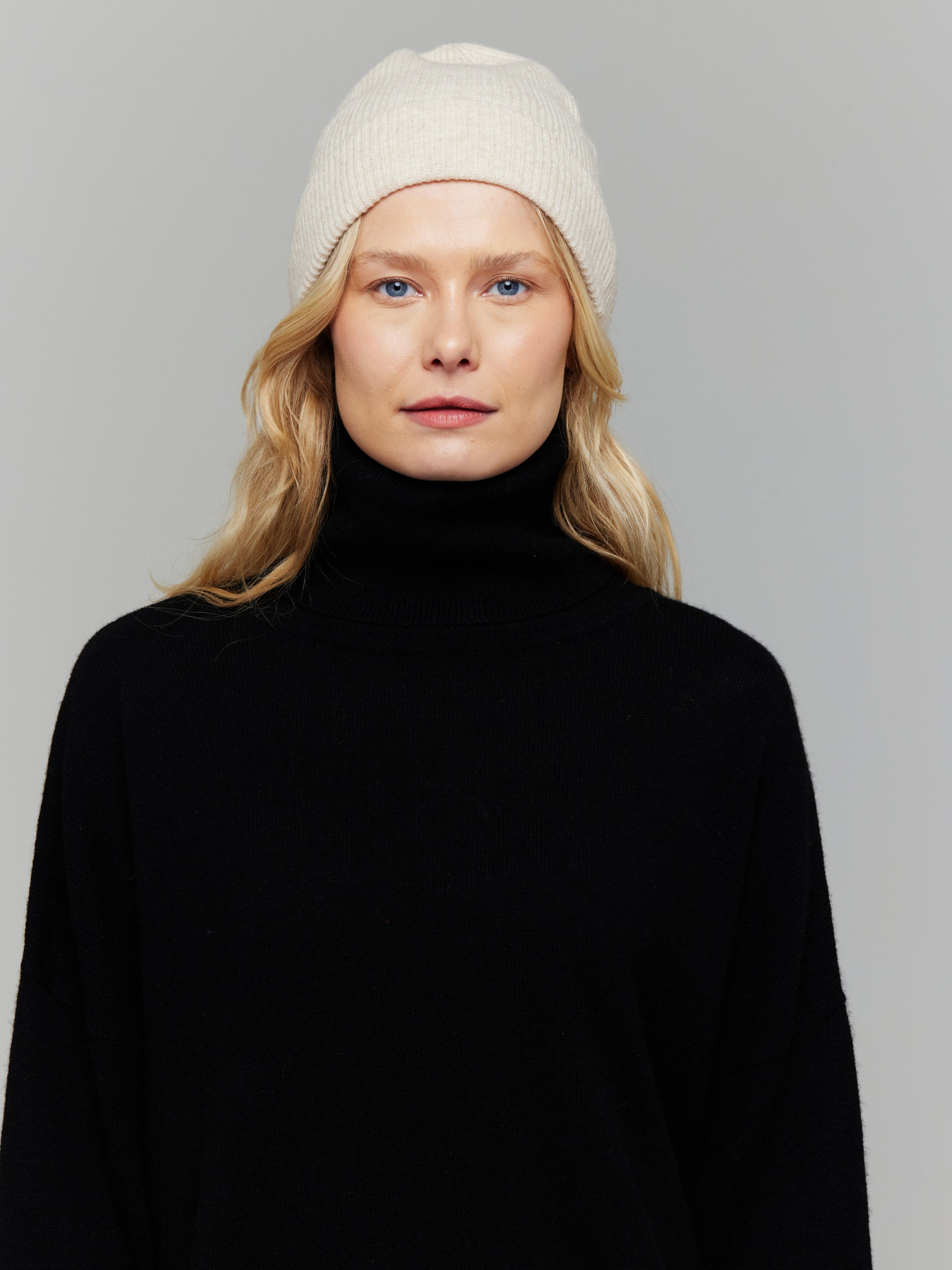 Woman wearing a black turtleneck and white beanie against a gray background