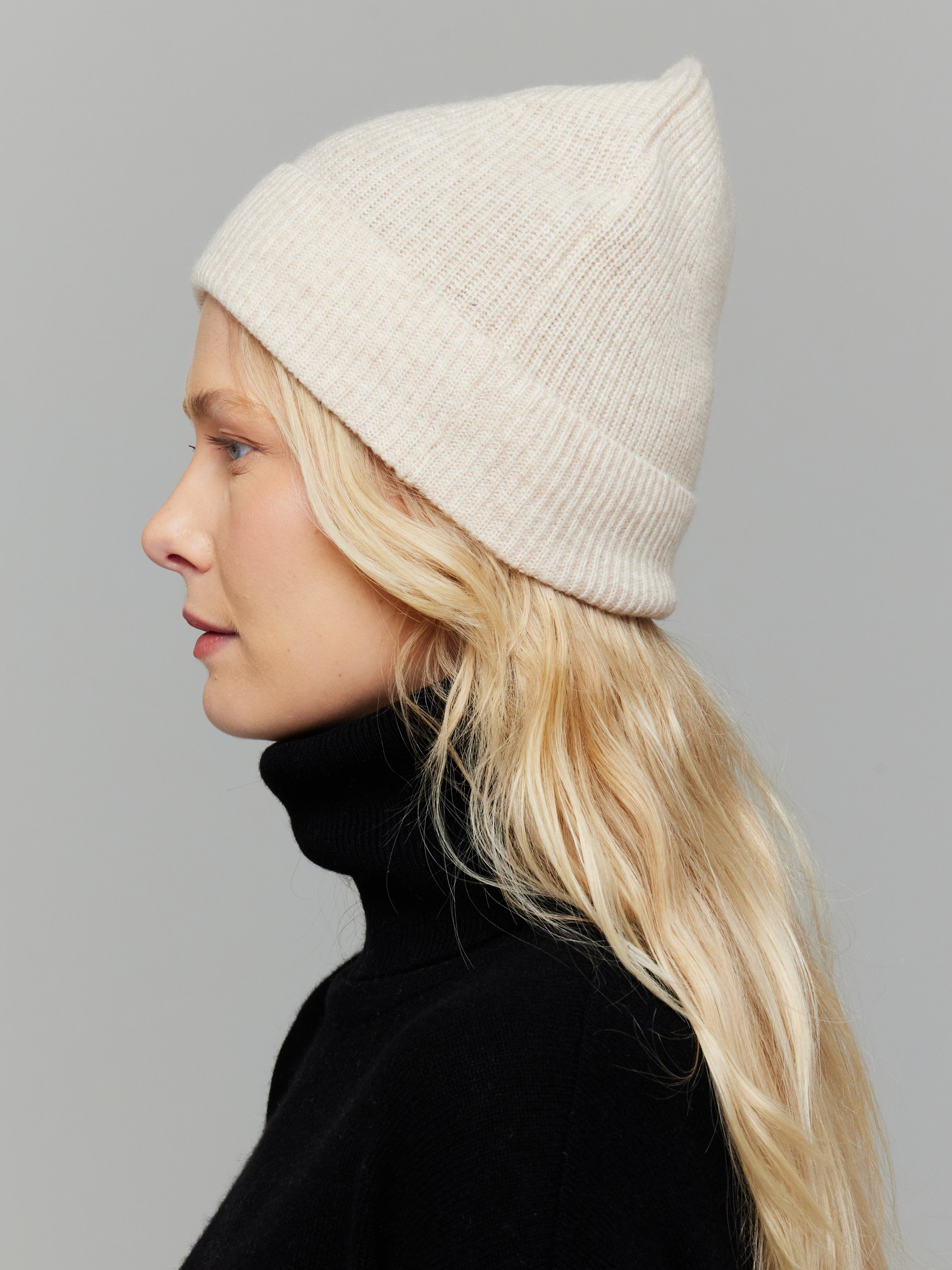 Person wearing a white beanie and black turtleneck against a gray background