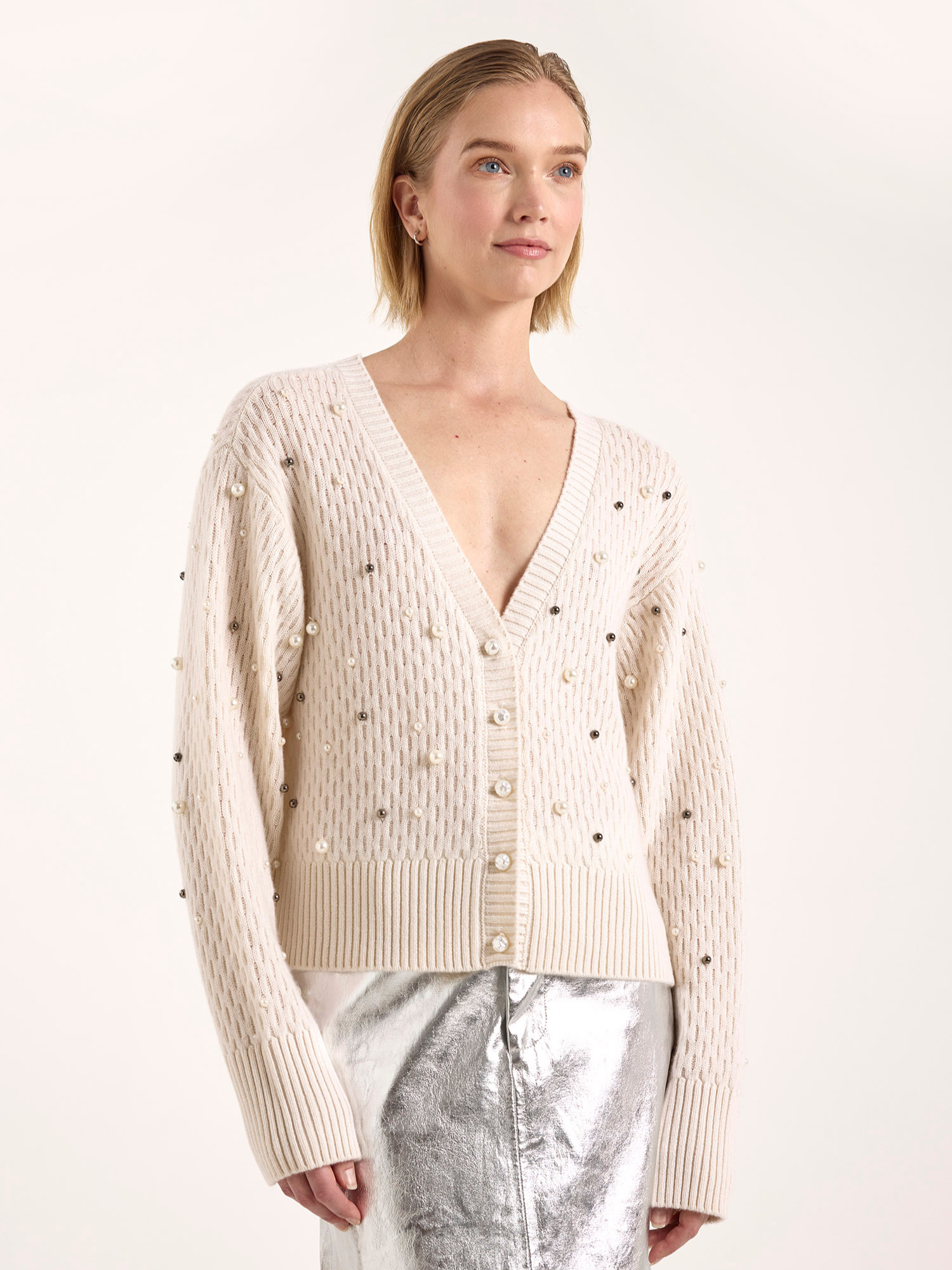 Woman wearing a beige cashmere cardigan with pearl buttons on a white background
