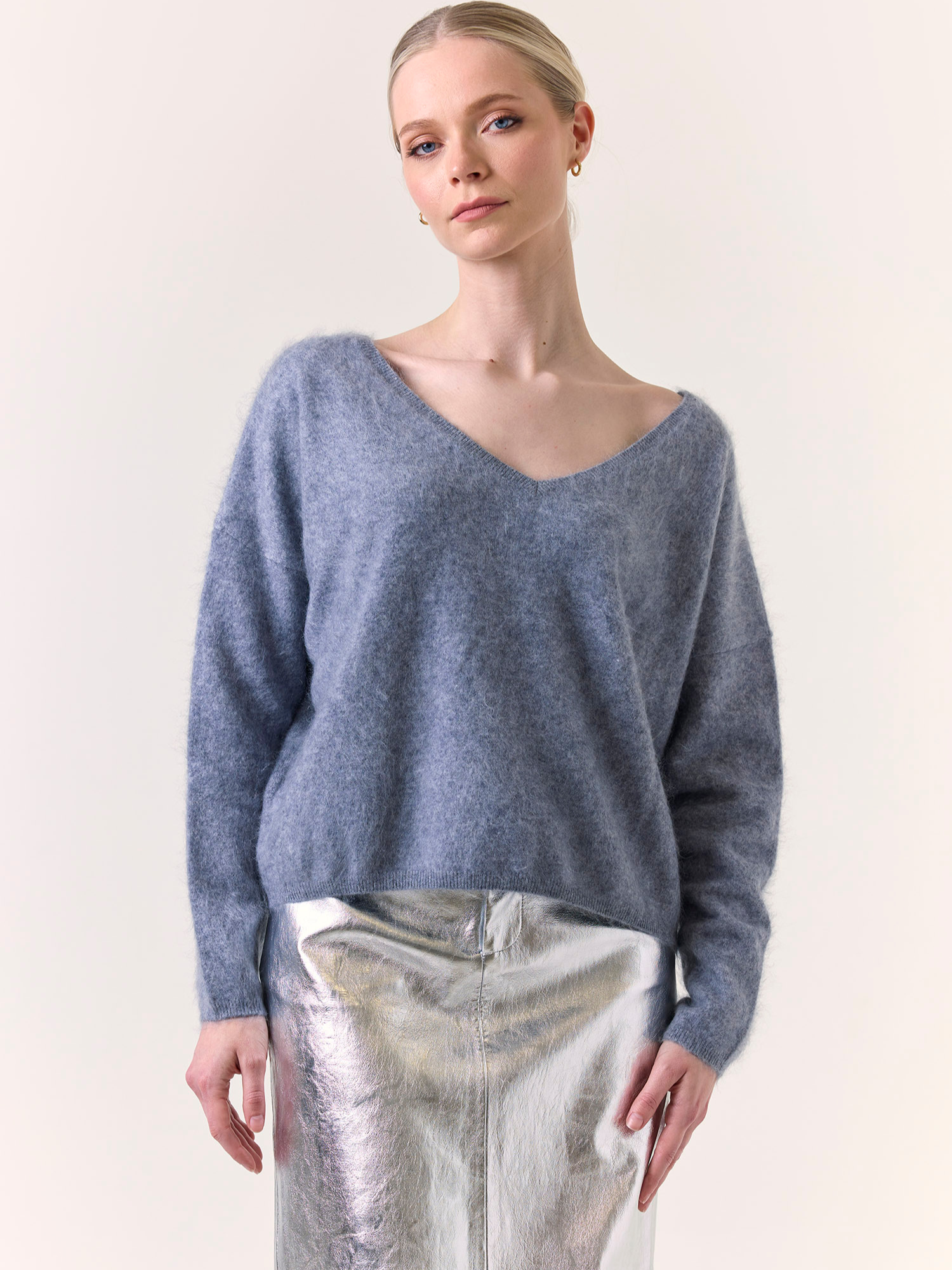 Woman wearing a blue sweater and silver pants against a white background