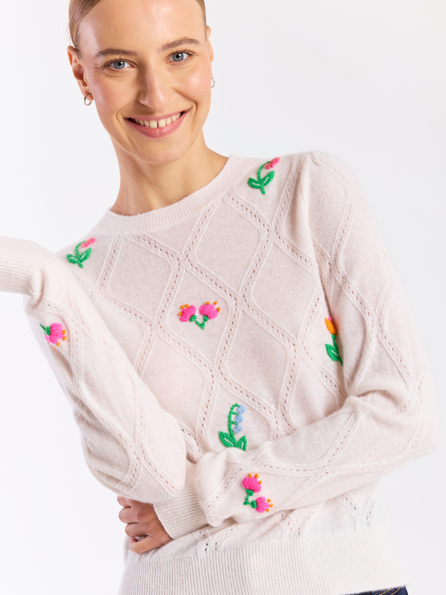 Woman wearing a cream sweater with floral embroidery on a white background