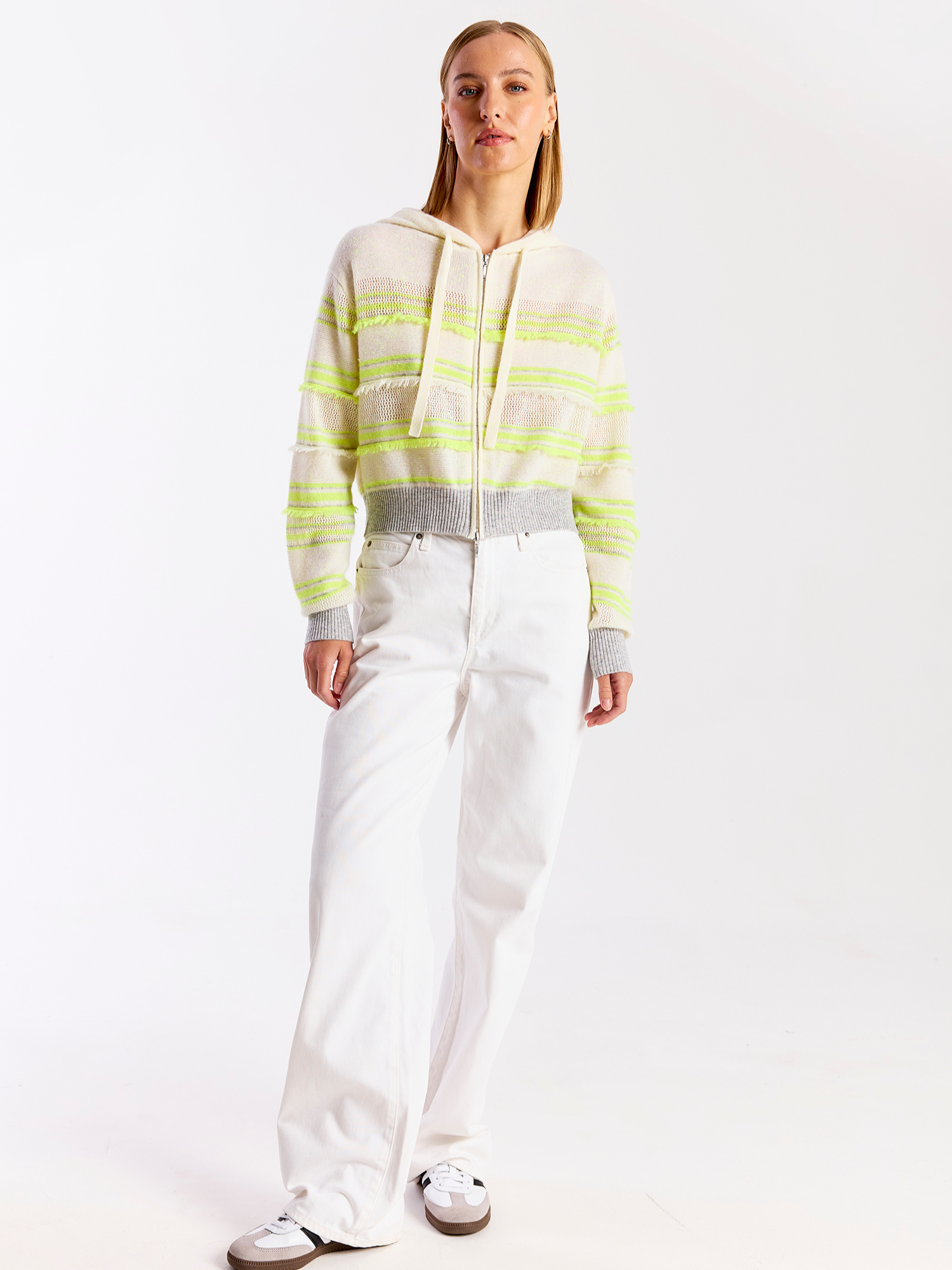 Person wearing a striped hoodie and white pants on a plain background