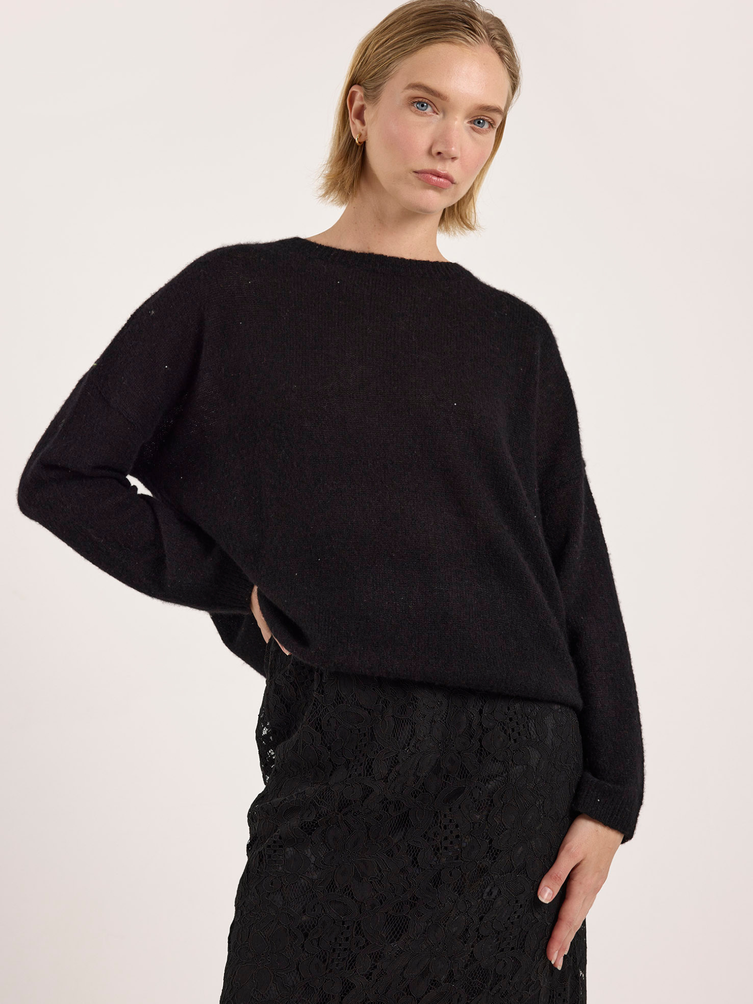 Woman wearing a black cashmere sweater and black skirt against a white background