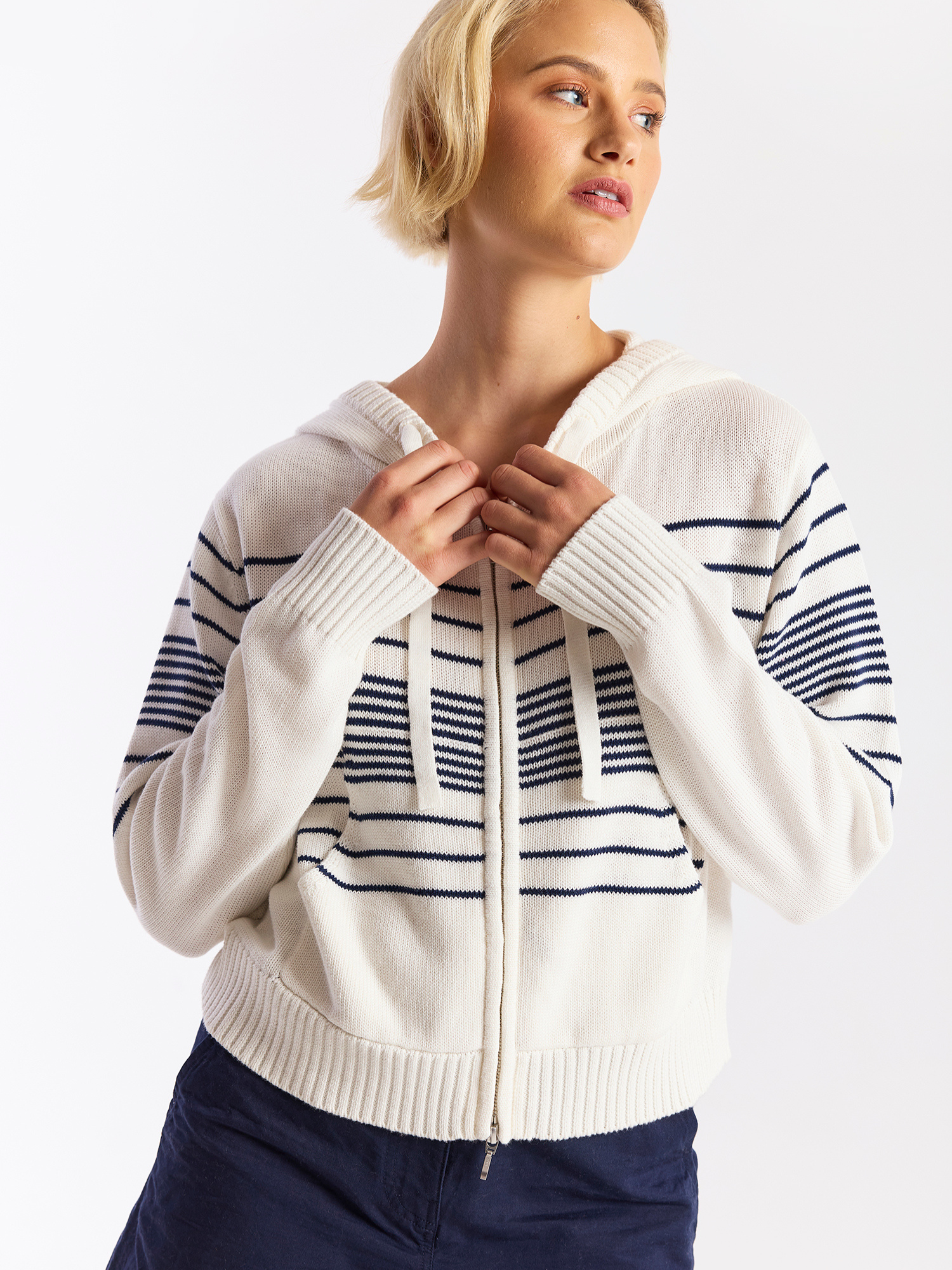 Woman wearing a white zip-up hoodie with blue stripe details on a plain background