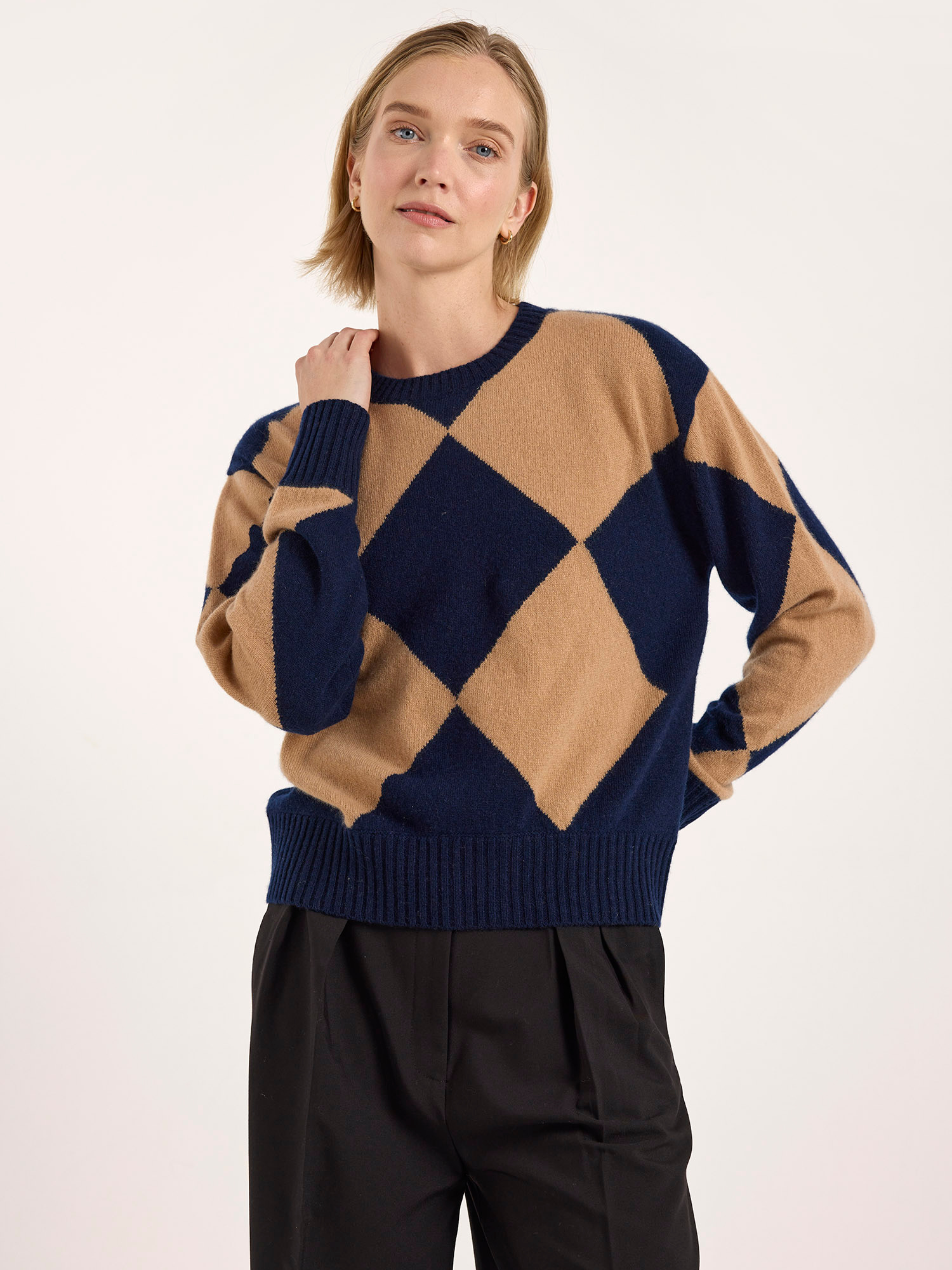 Person wearing a beige and navy diamond pattern sweater on a white background