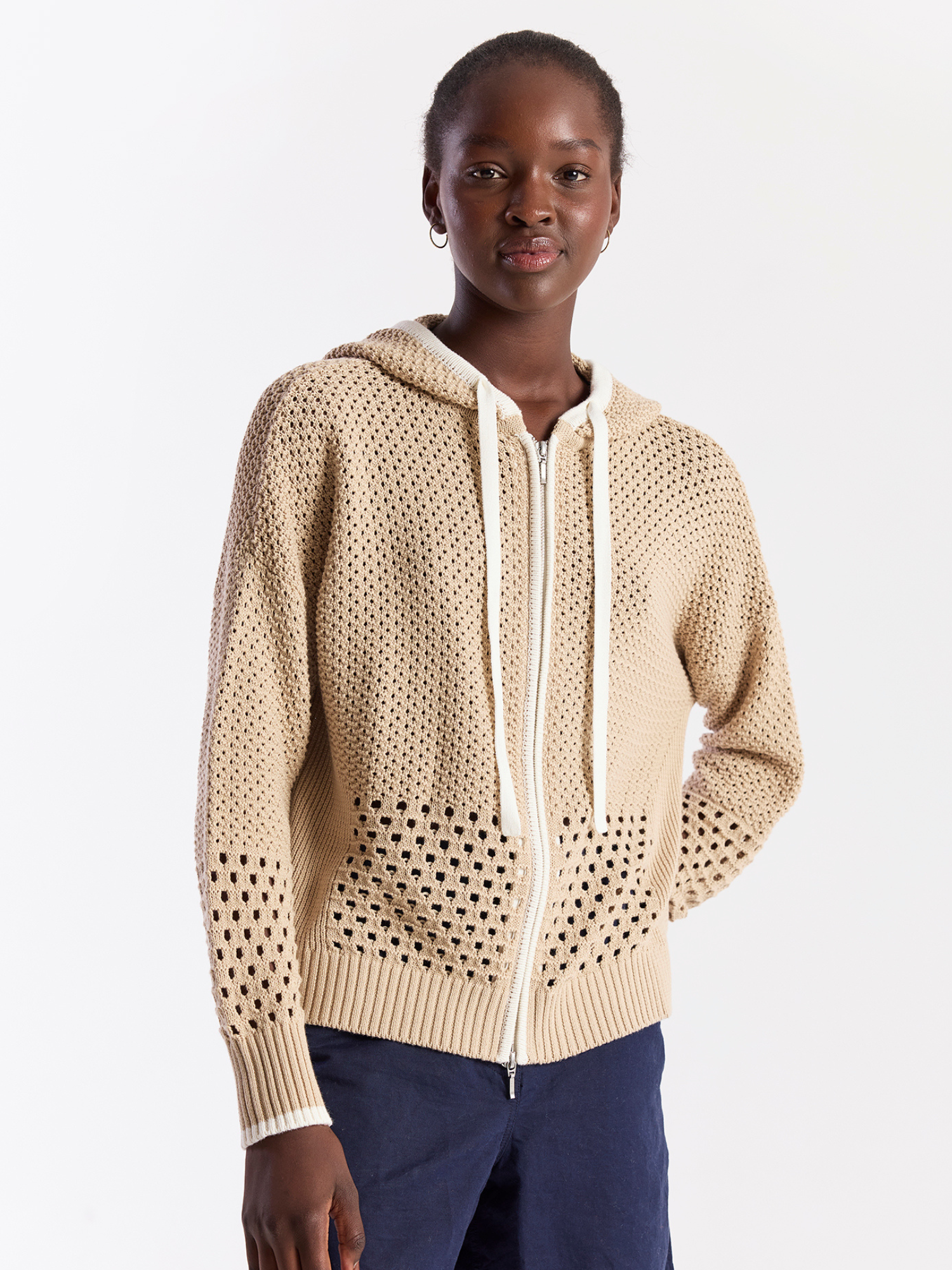 Woman wearing a beige knitted hoodie with a white zipper on a plain background
