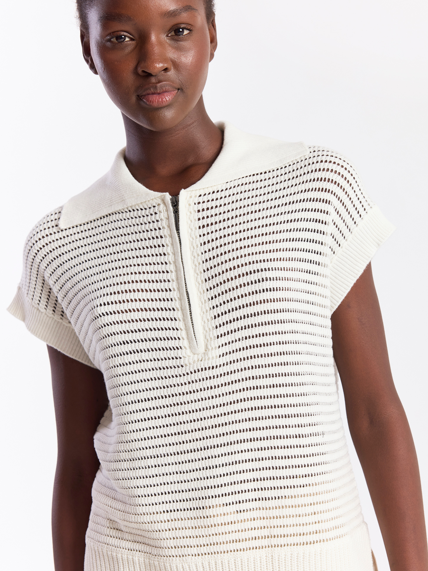 Woman wearing a white knit top with a subtle pattern on a plain background