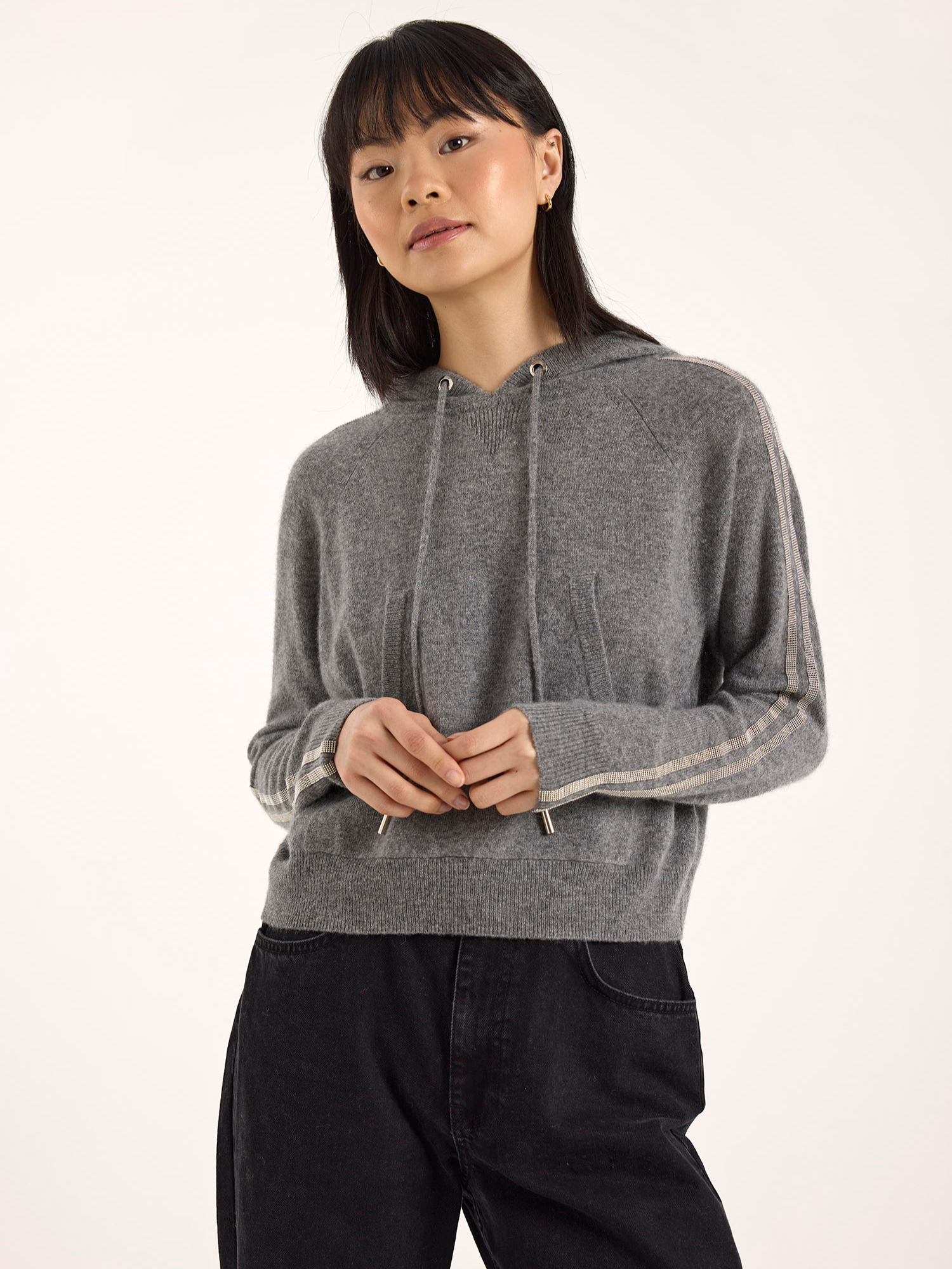 Woman wearing a gray cashmere hoodie with white trim on a white background