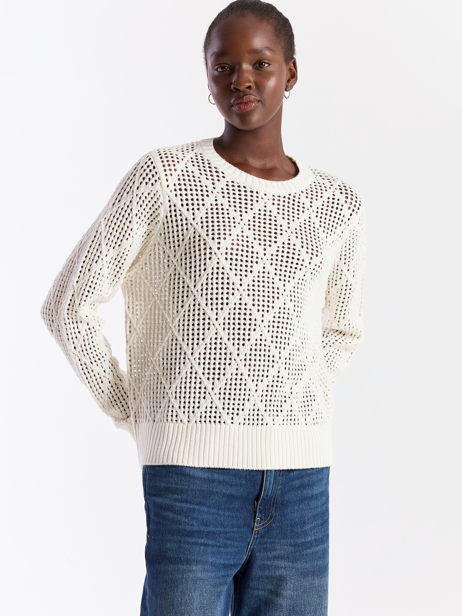 Woman wearing a white textured sweater and blue jeans on a white background