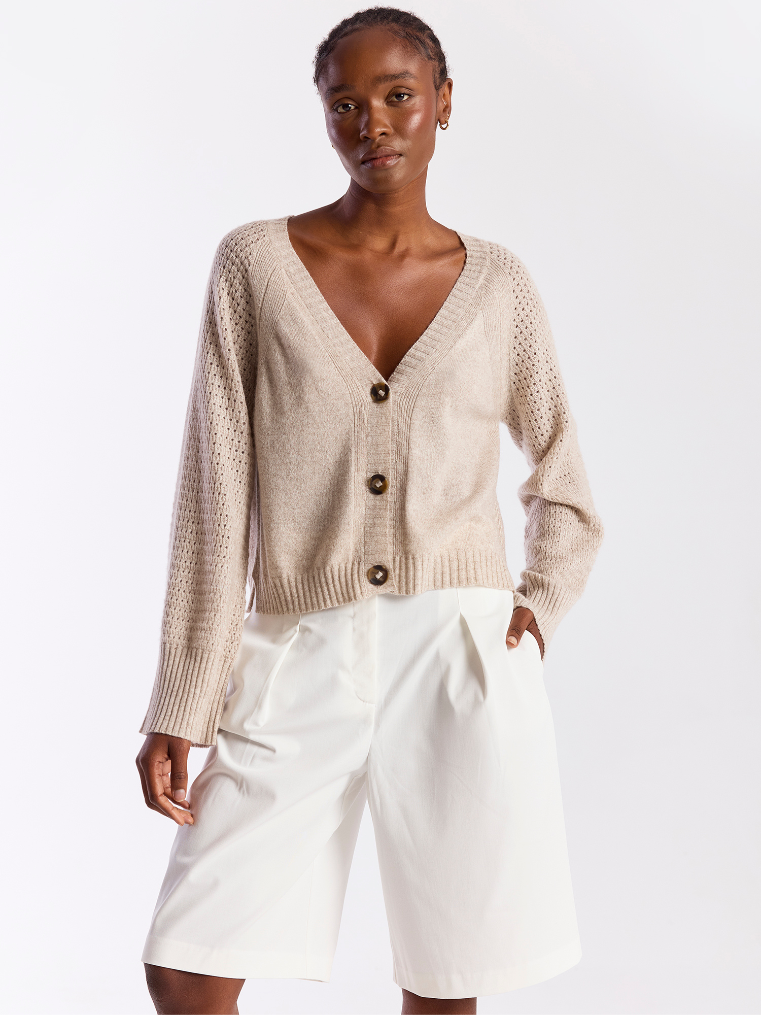 Woman wearing a beige cardigan and white shorts on a white background