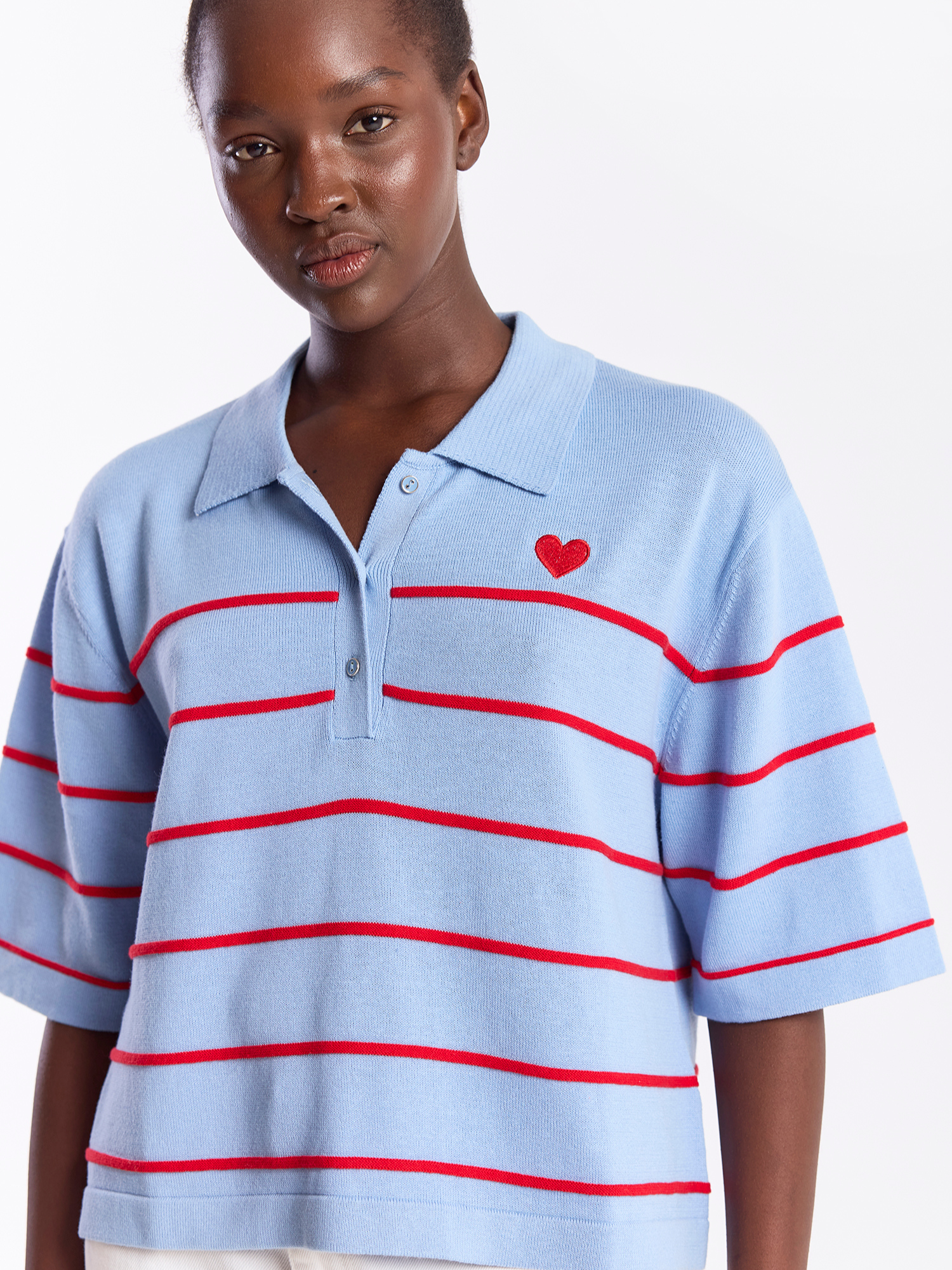 Woman wearing a light blue polo shirt with red stripes and a red heart on a white background