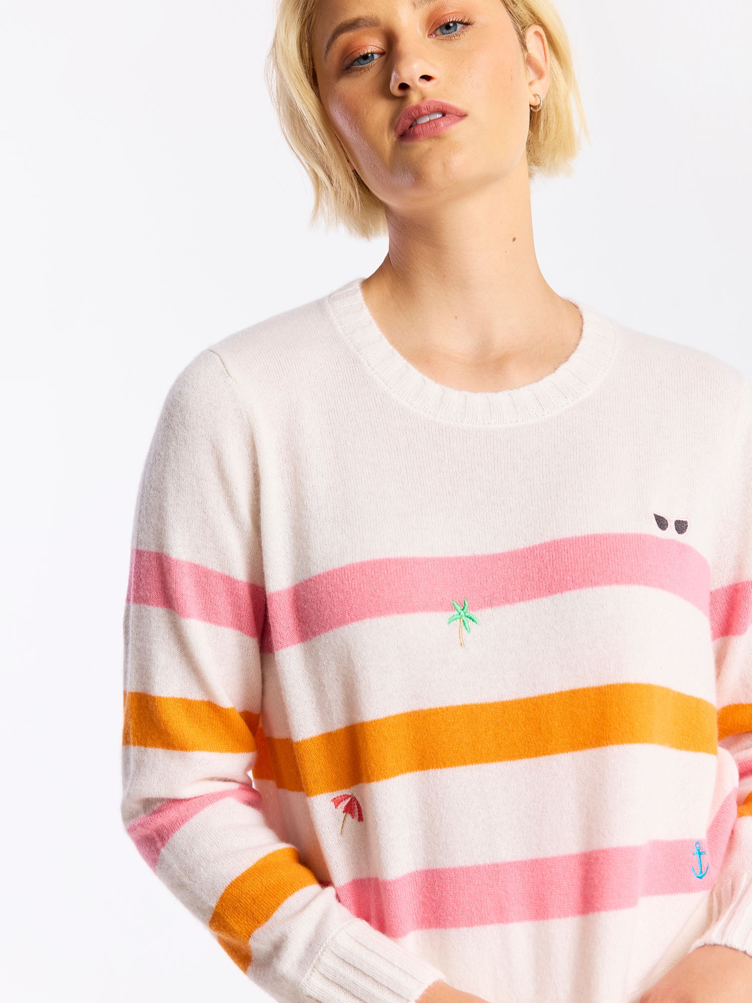 Woman wearing a striped cashmere sweater with pink and orange horizontal stripes on a white background