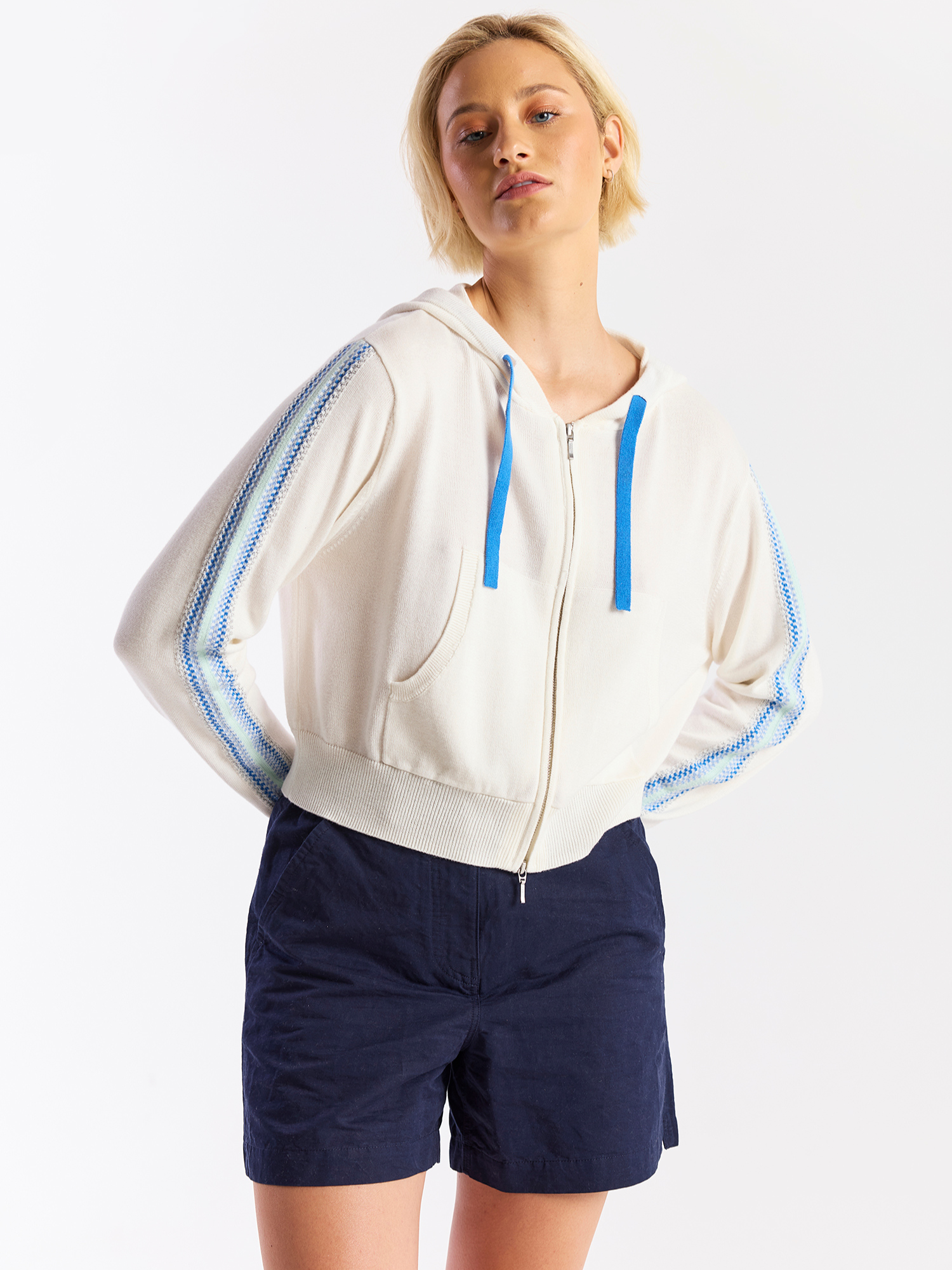 Woman wearing a white hoodie with blue accents and navy shorts on a white background