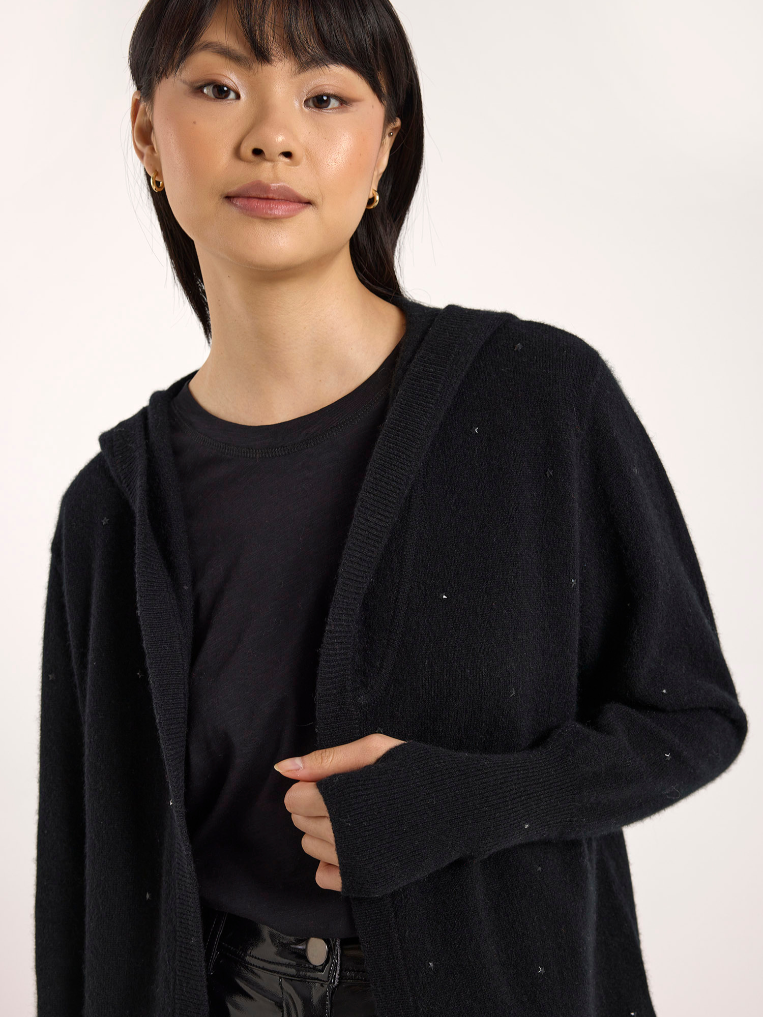 Person wearing a black cardigan over a black shirt on a white background