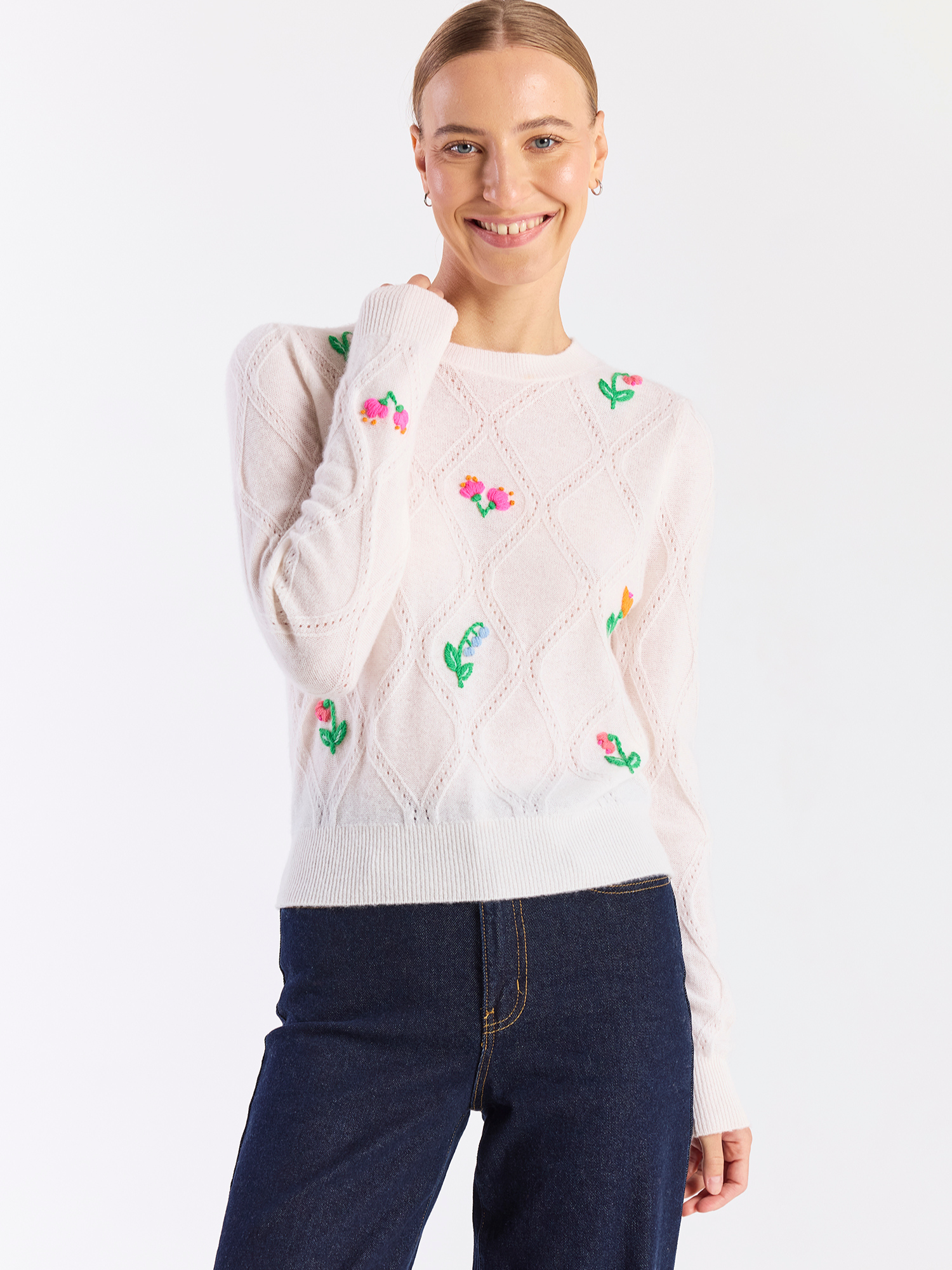 Woman wearing a cream sweater with floral patterns on a white background