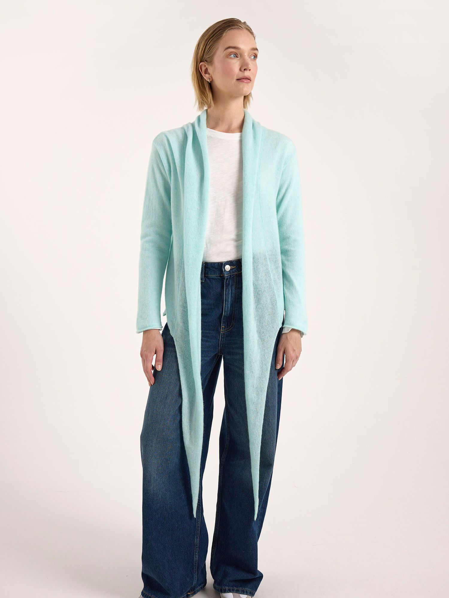 Person wearing a light blue cardigan over a white shirt and dark jeans on a white background