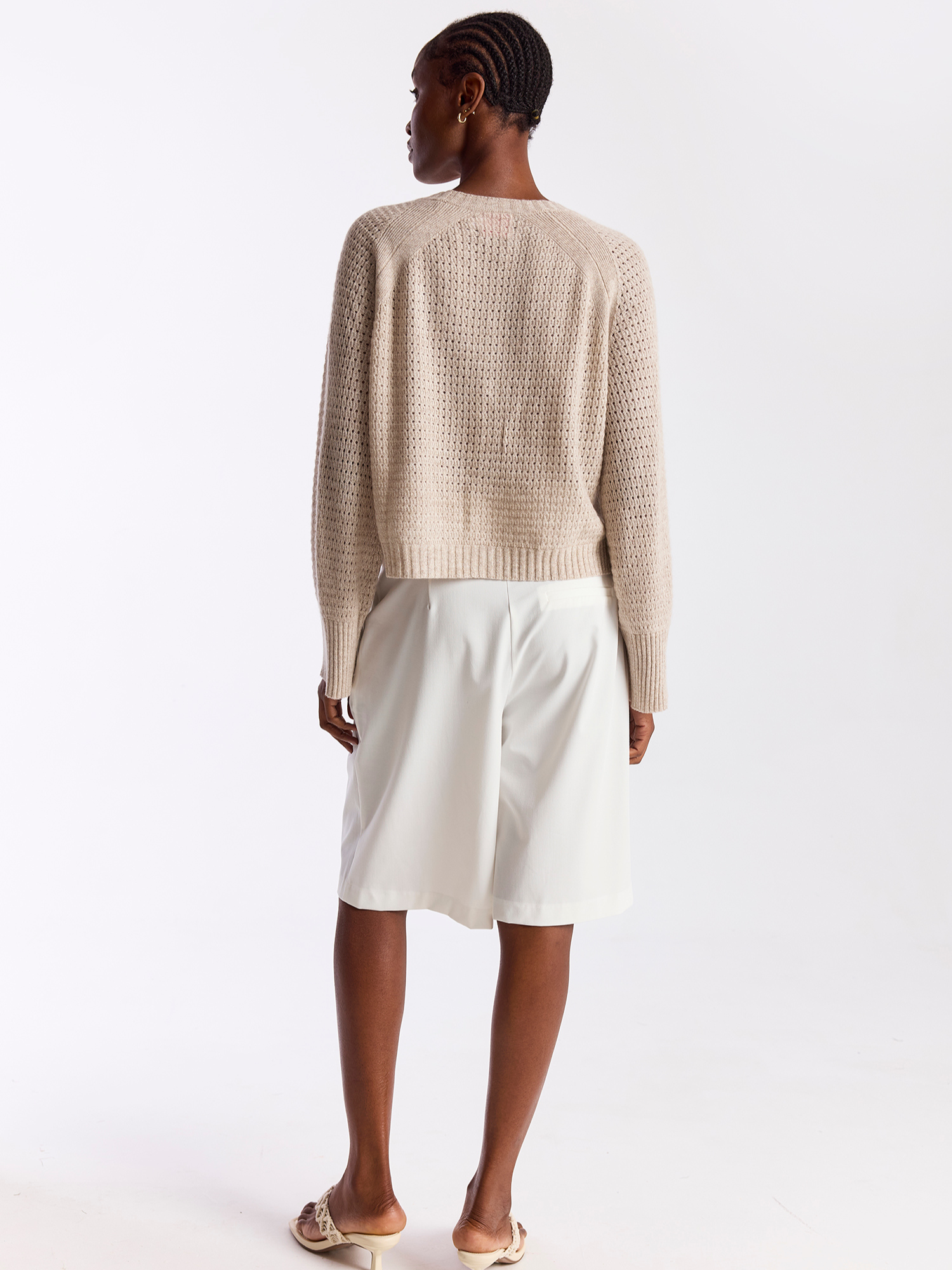 Person wearing a beige knitted sweater and white skirt on a white background