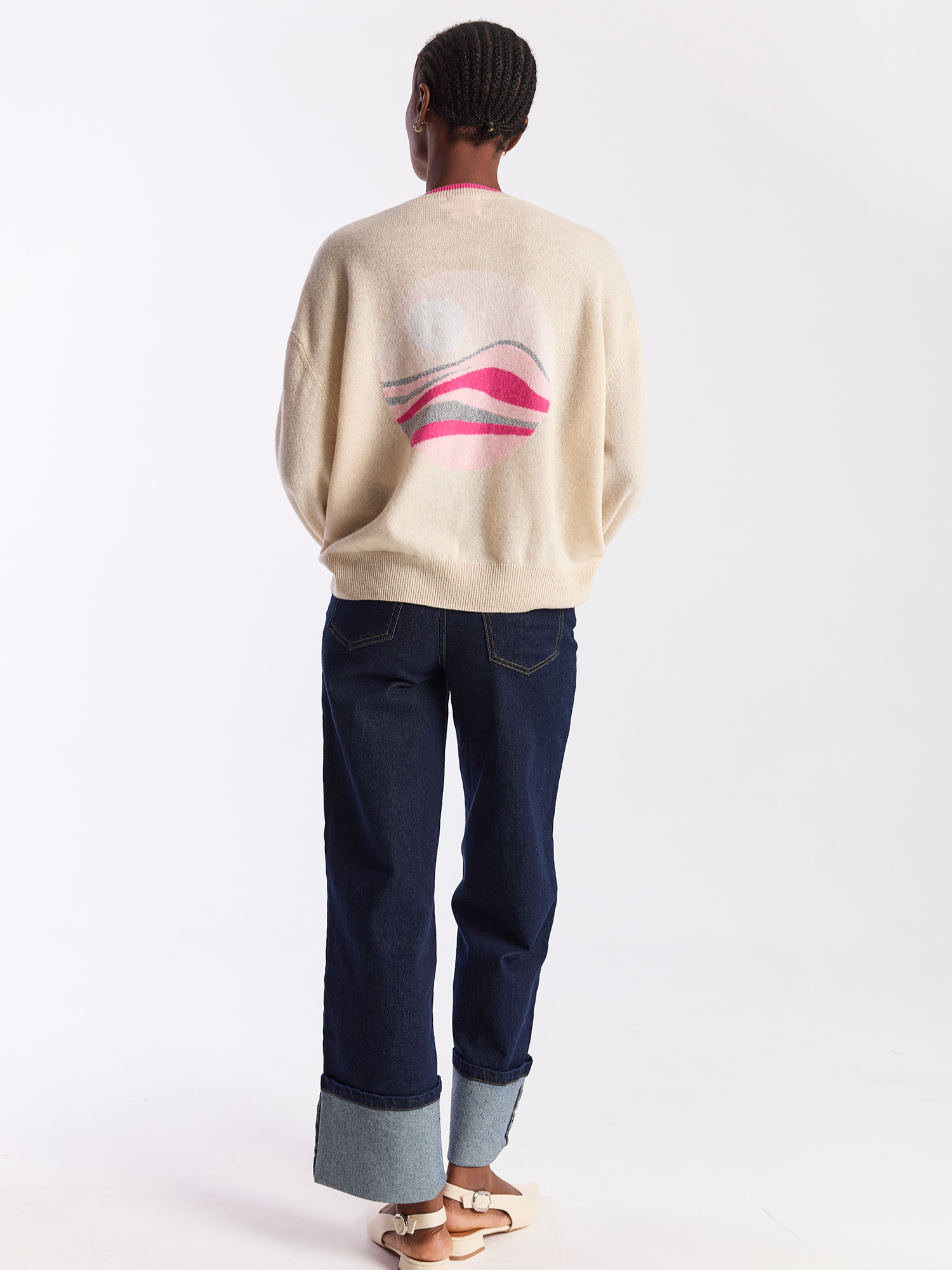 Person wearing a beige sweater with a graphic design and dark blue jeans on a white background