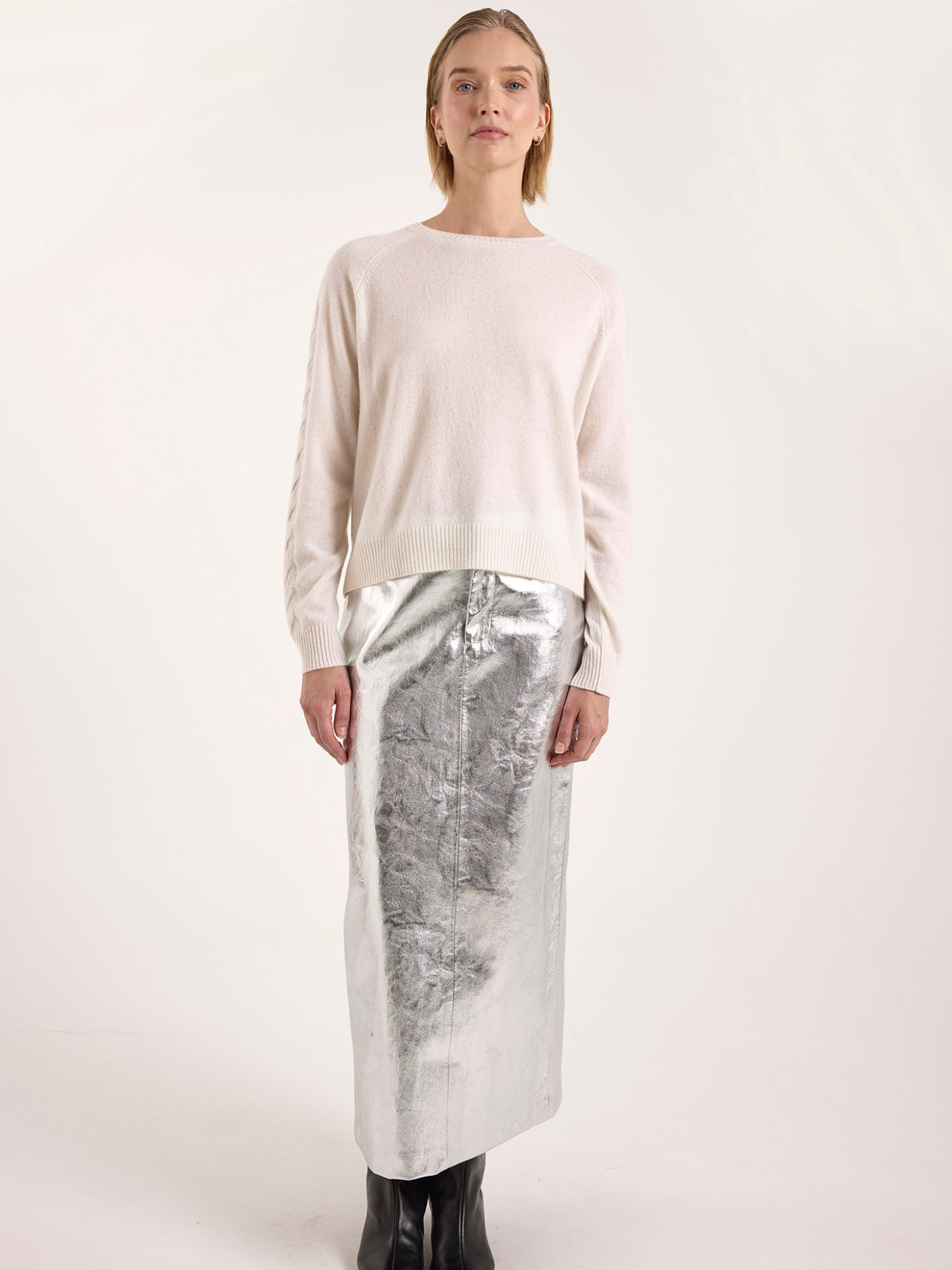 Woman wearing a white cashmere sweater and silver metallic skirt on a white background