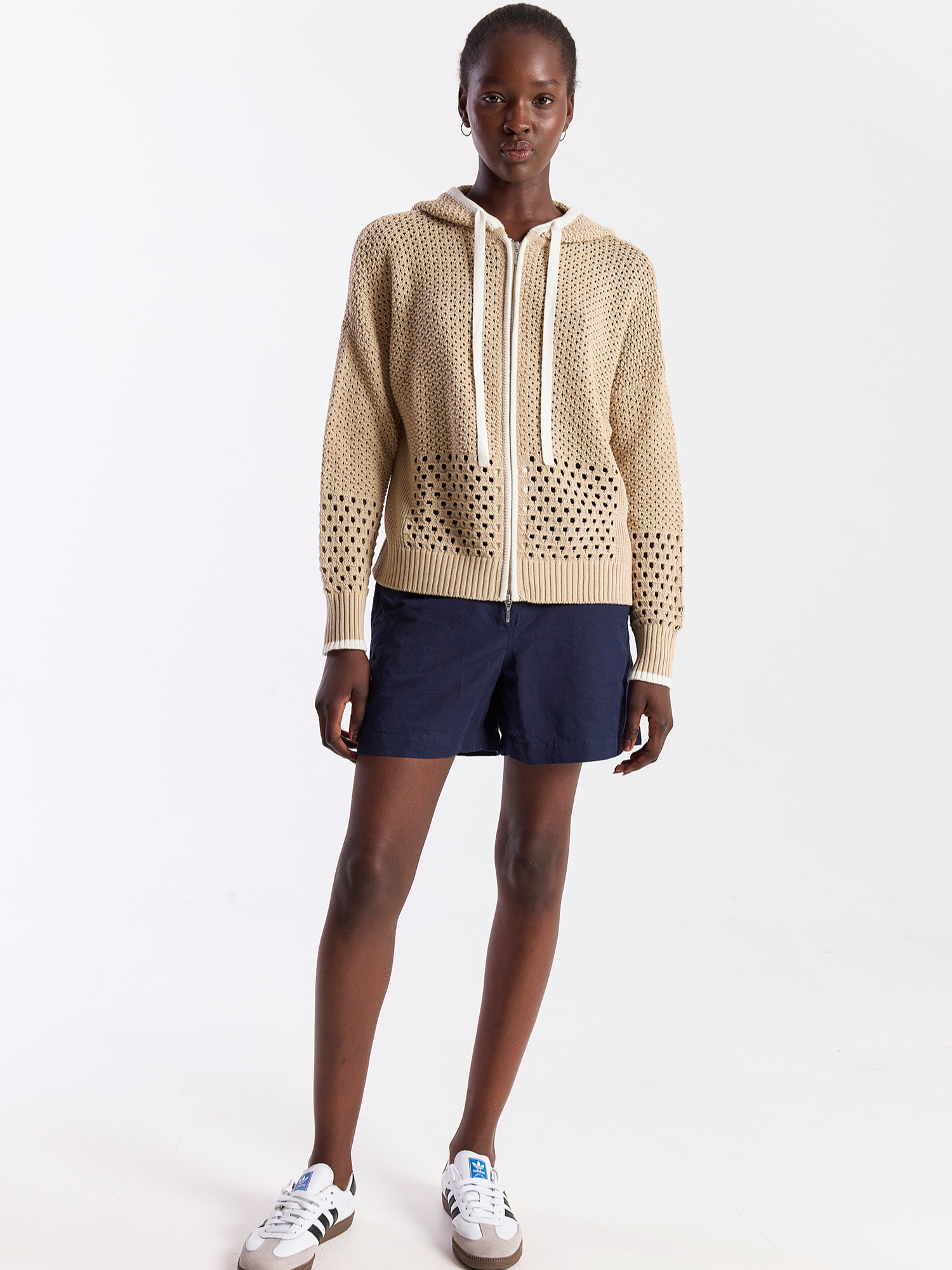 Person wearing a beige knitted hoodie with a white background