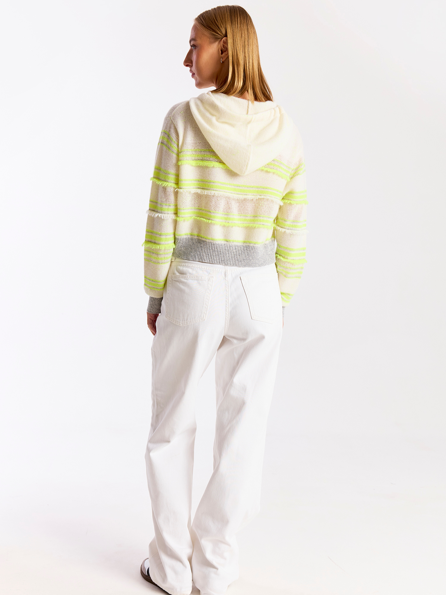 Person wearing a striped hoodie and white pants on a light gray background