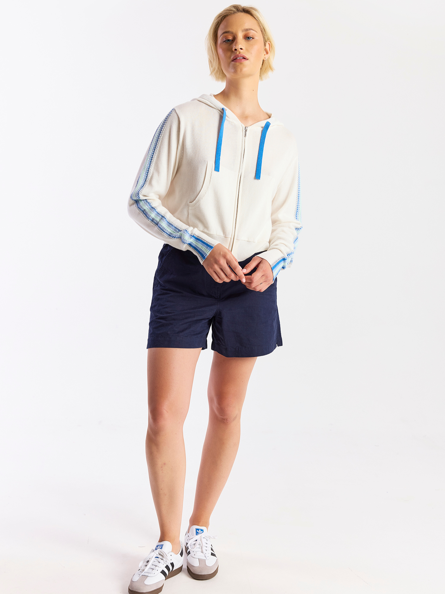 Person wearing a white jacket with blue accents and navy shorts on a white background