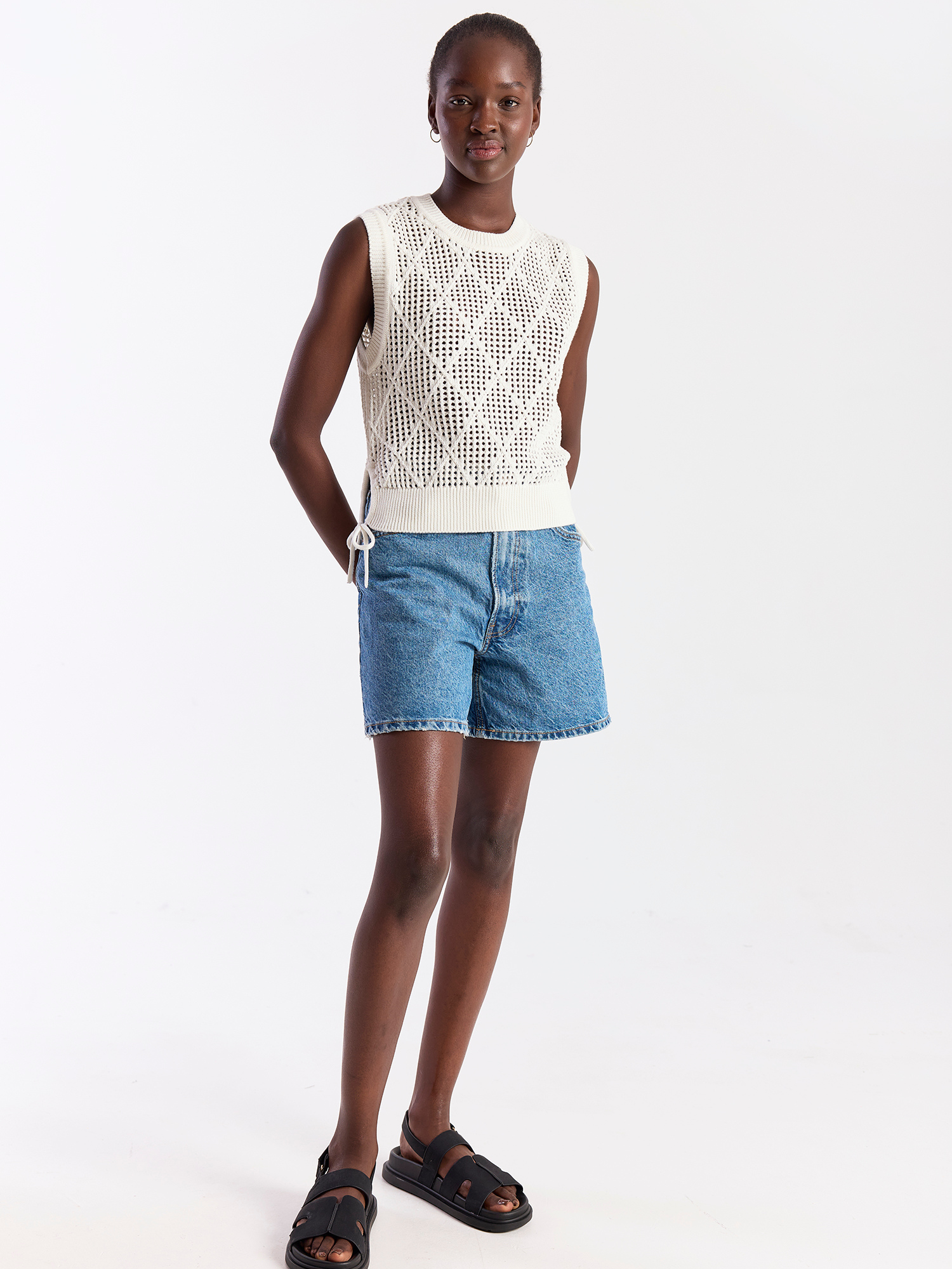 Woman wearing a white sleeveless top and blue denim shorts on a white background