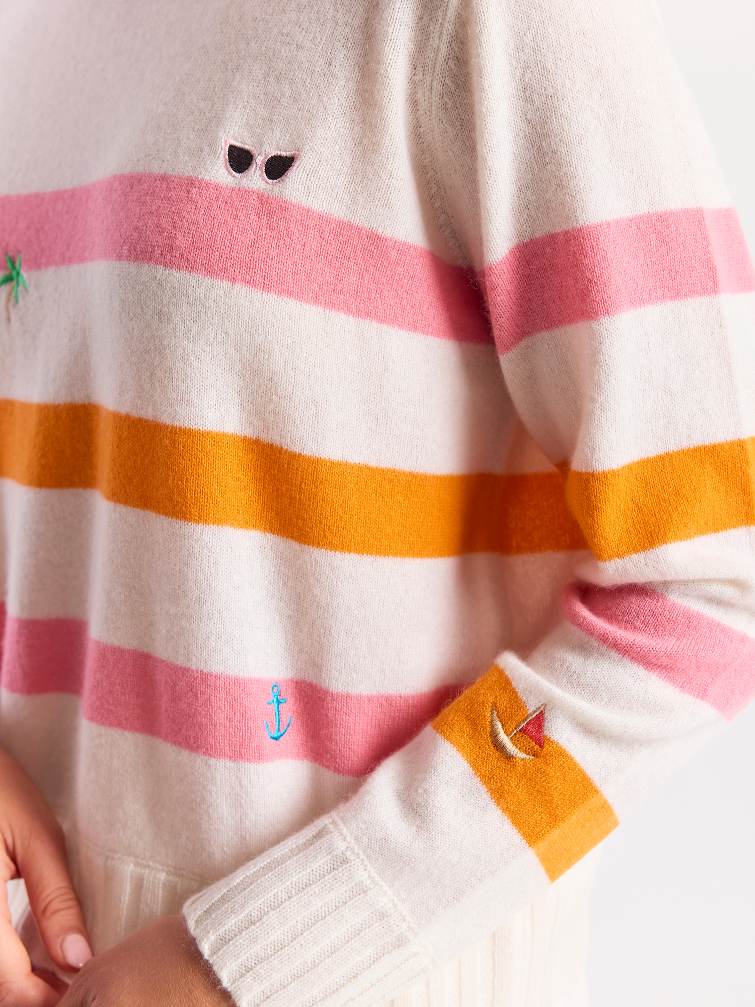 Woman wearing a striped cashmere sweater with pink and orange horizontal stripes on a white background