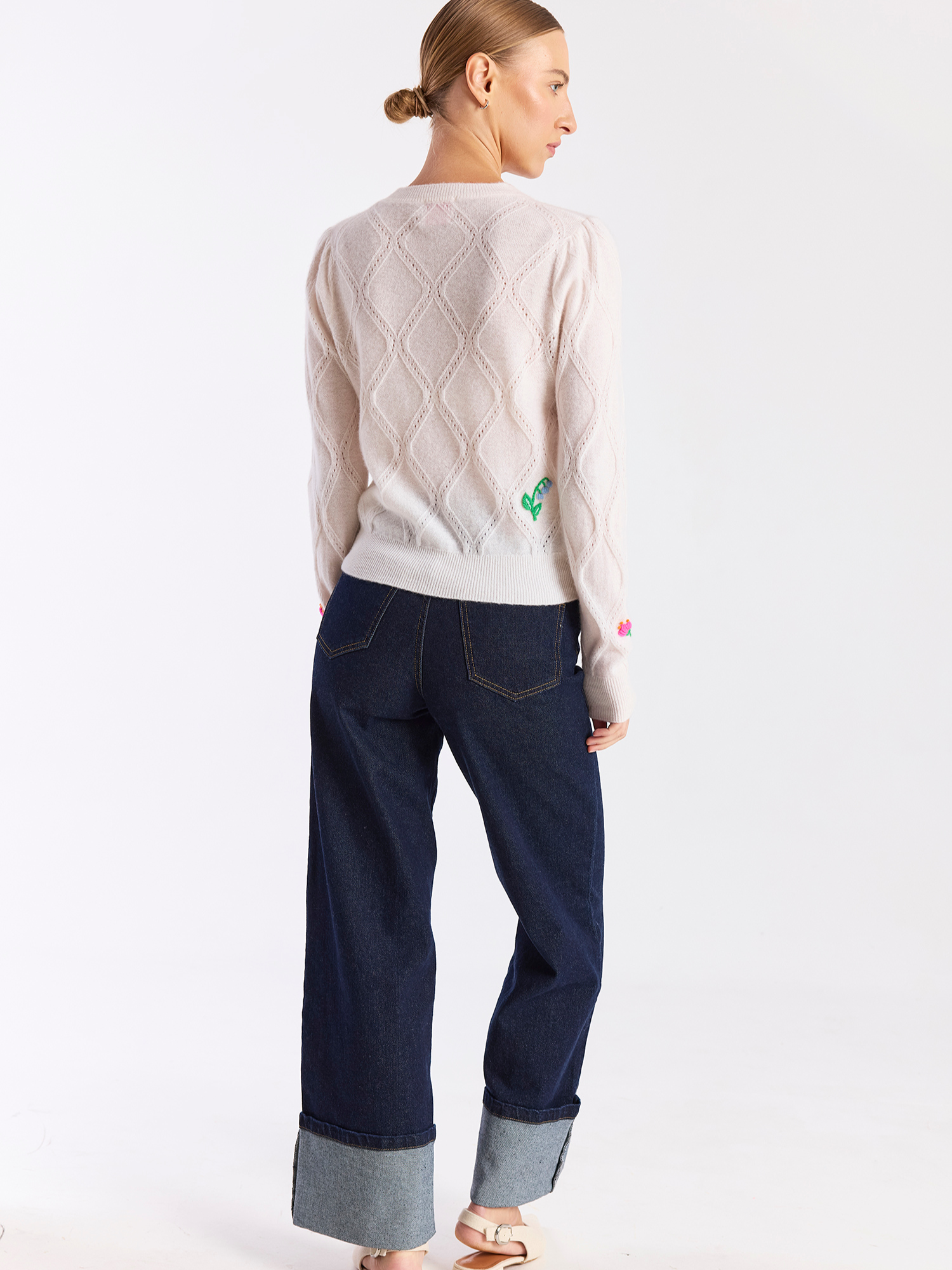 Person wearing a light-colored sweater and dark blue jeans on a white background