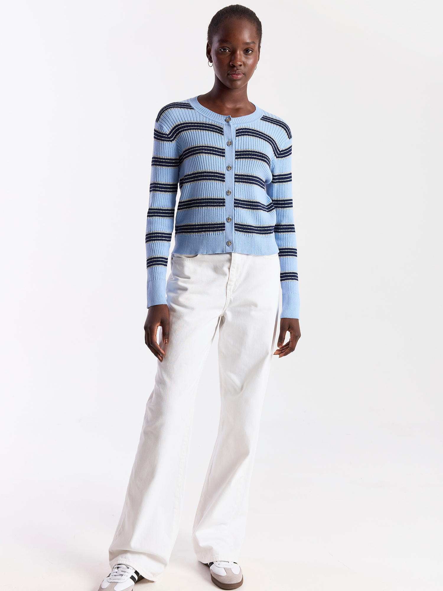 Person wearing a blue and white striped cardigan with white pants on a white background