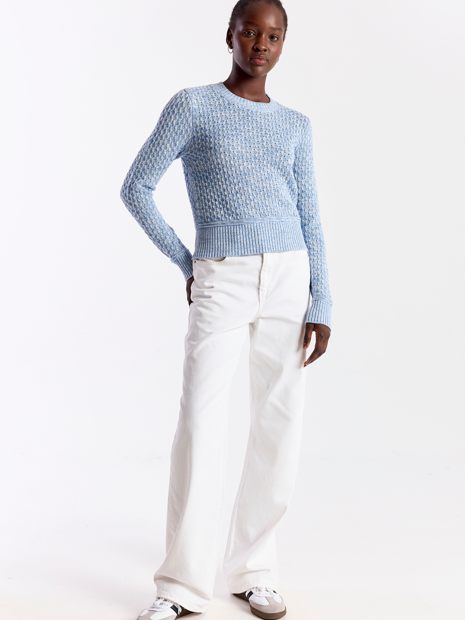 Person wearing a light blue textured sweater and white pants on a white background