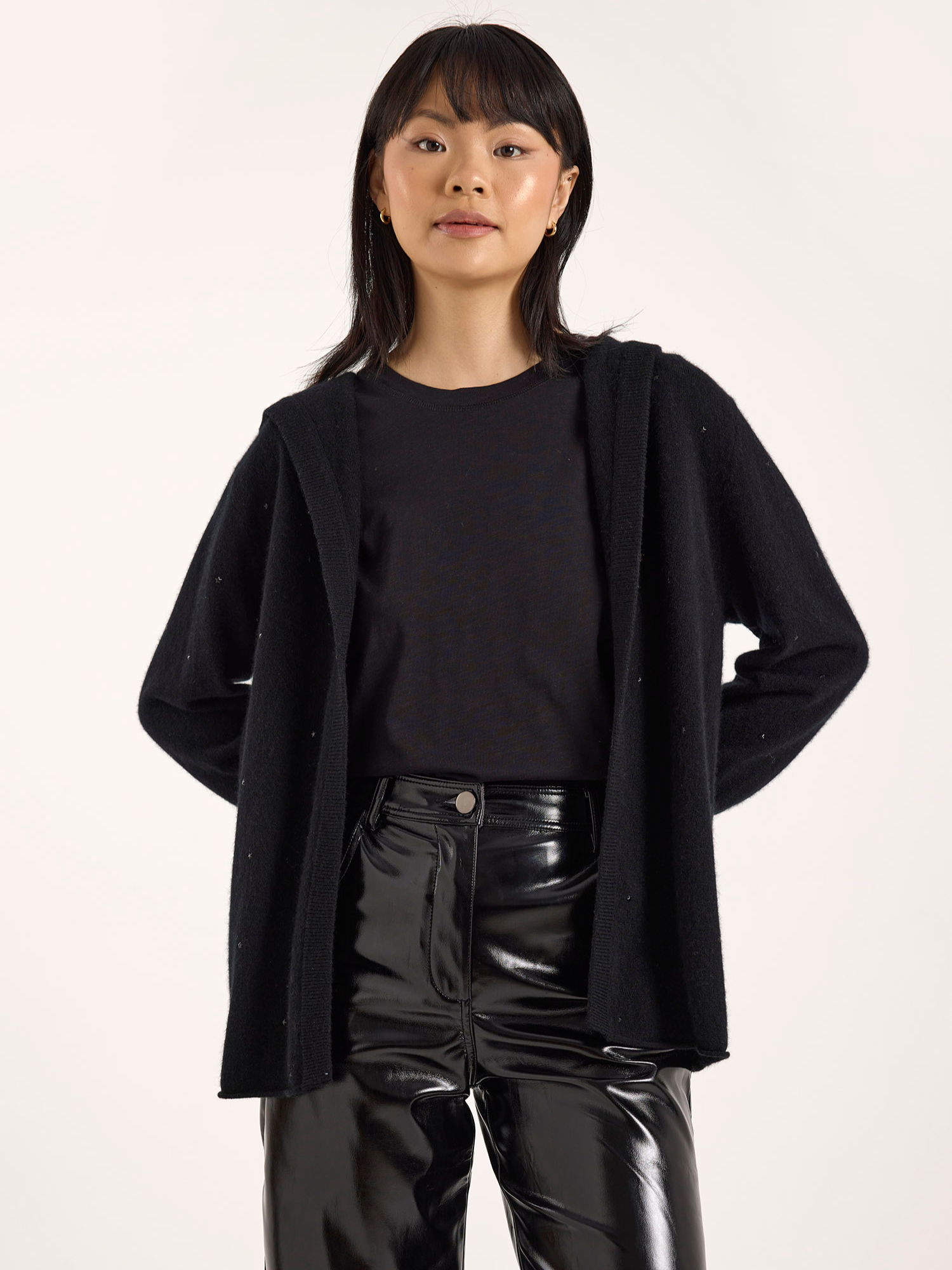 Person wearing a black cardigan, black shirt, and shiny black pants on a white background