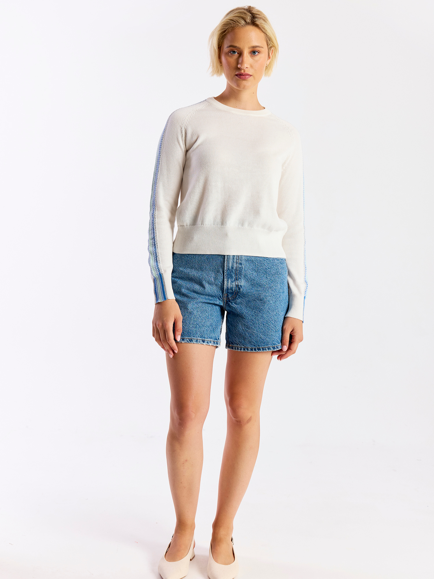 Woman wearing a white sweater and denim shorts on a white background