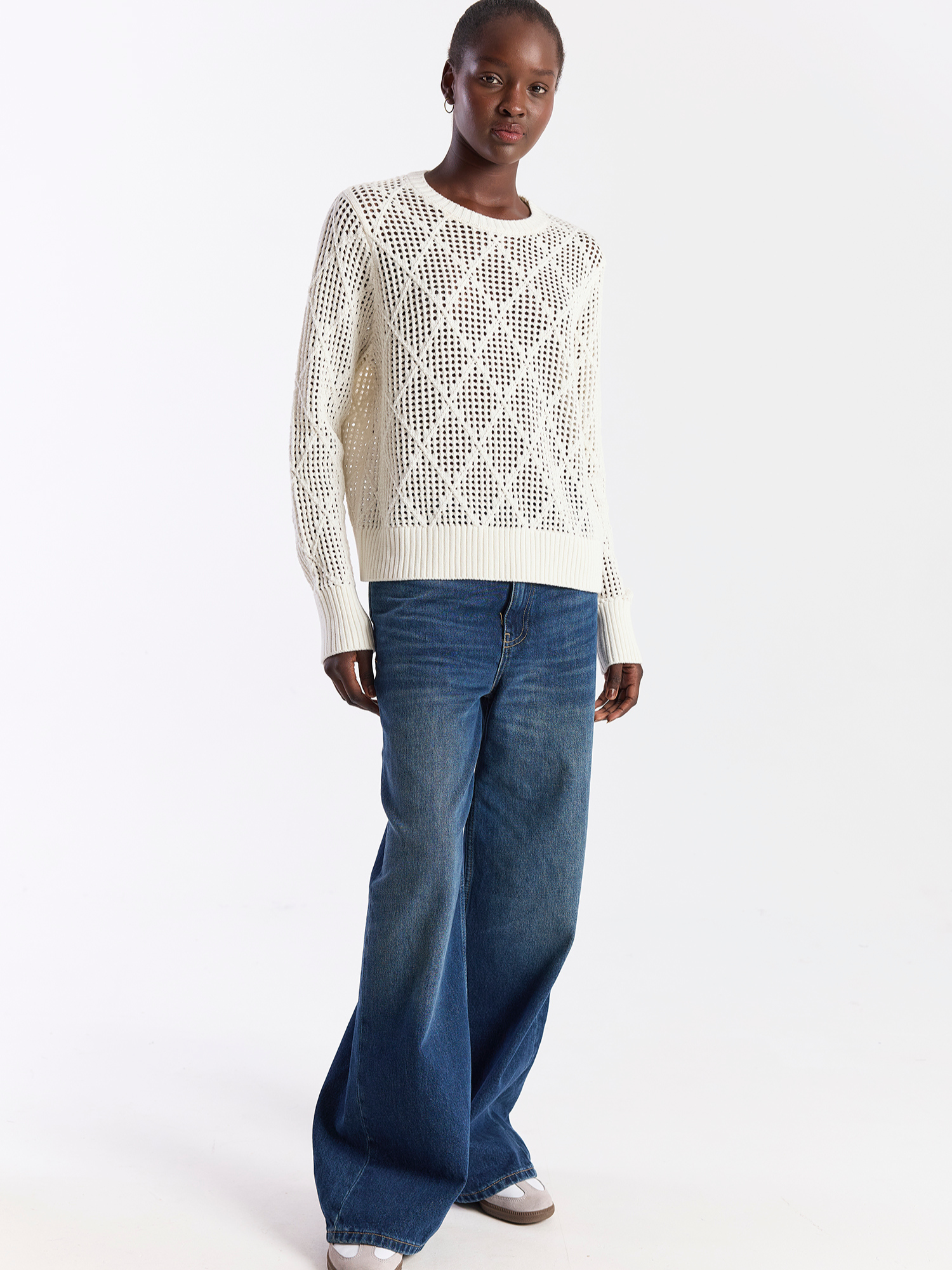 Person wearing a white knit sweater and blue jeans on a white background