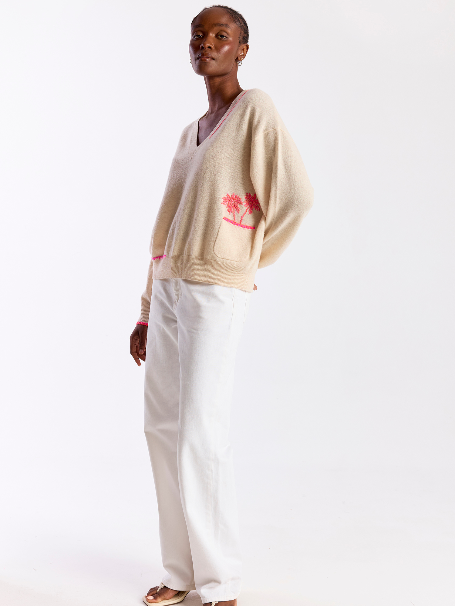 Woman wearing a beige cardigan with a floral design and white pants on a white background